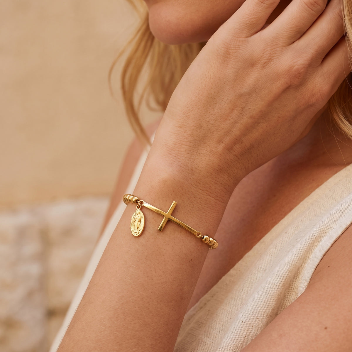 Woman wearing the gold-tone beaded bracelet with horizontal cross and religious medal charm on her wrist.