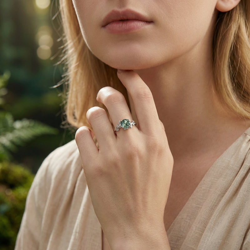 Silver moss agate floral crest ring worn on a woman's hand in a soft-focus forest lifestyle setting.