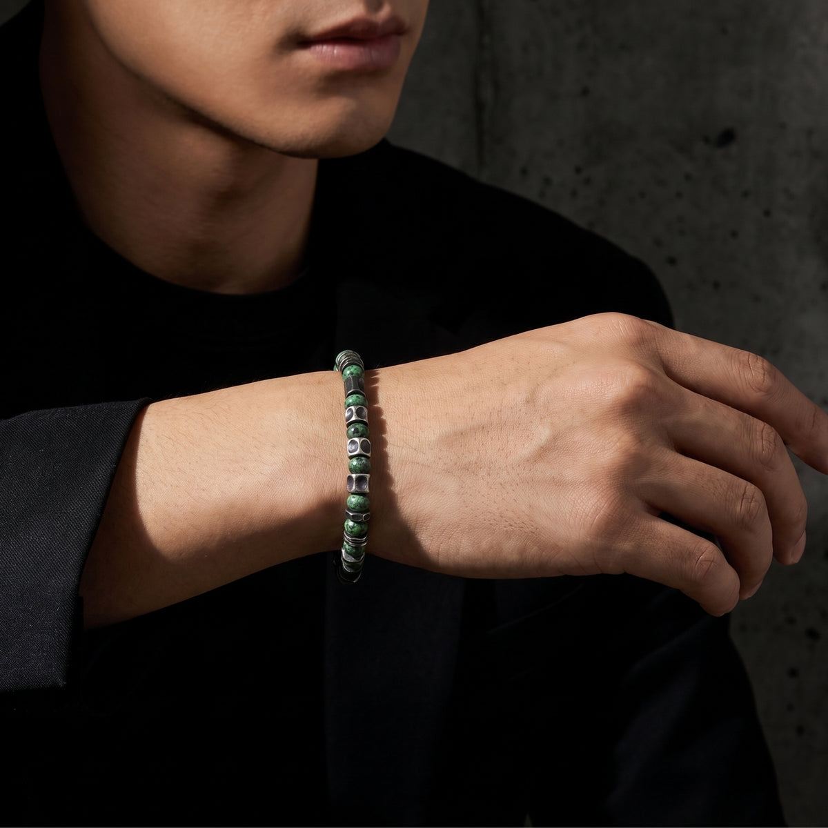Close view of a model wearing the green beaded and silver barrel spacer bracelet over a black outfit.