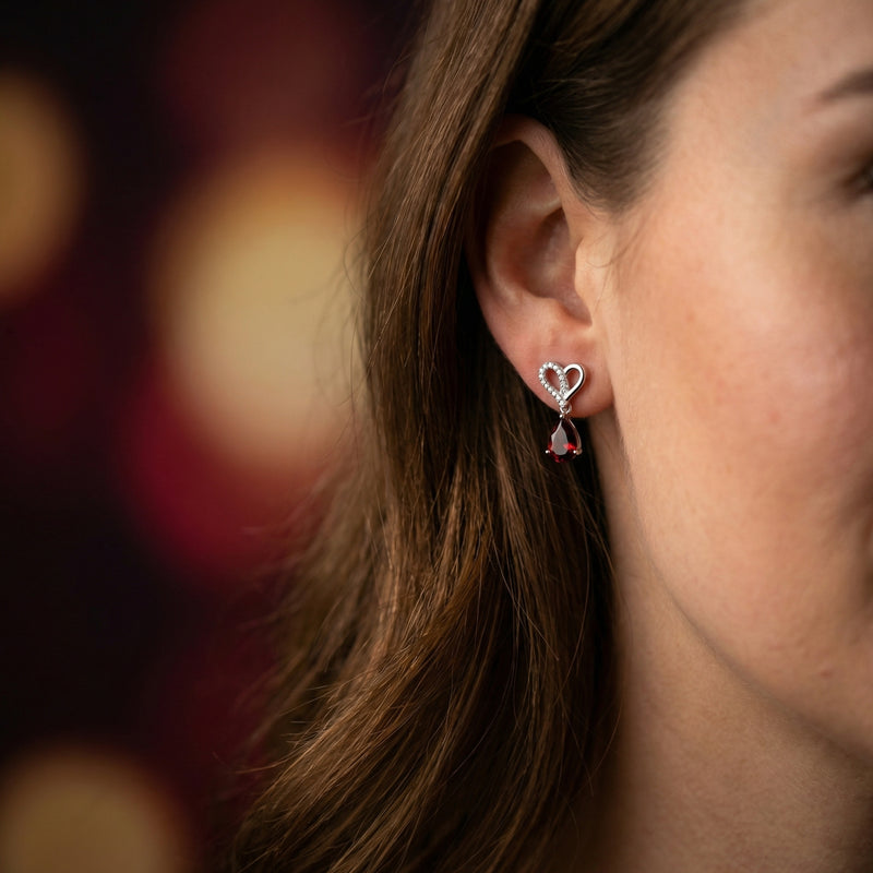 Model wearing a Lovisa white gold earring featuring a heart-shaped top and a pear-cut red garnet drop.
