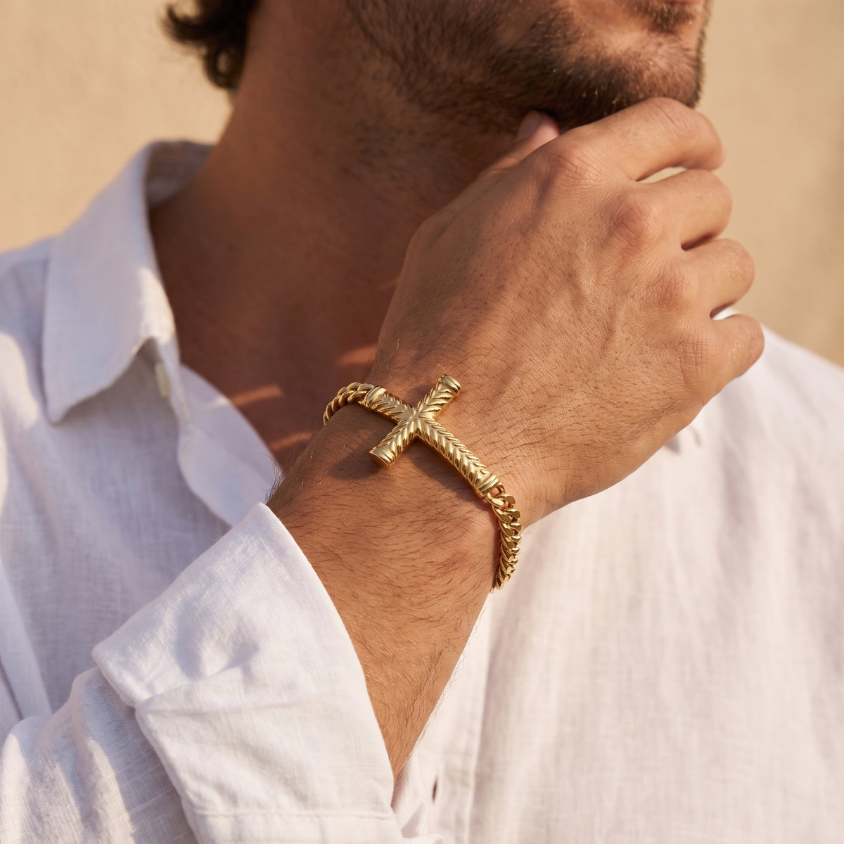 Gold-tone chevron cross bracelet worn on a man's wrist with a white shirt.