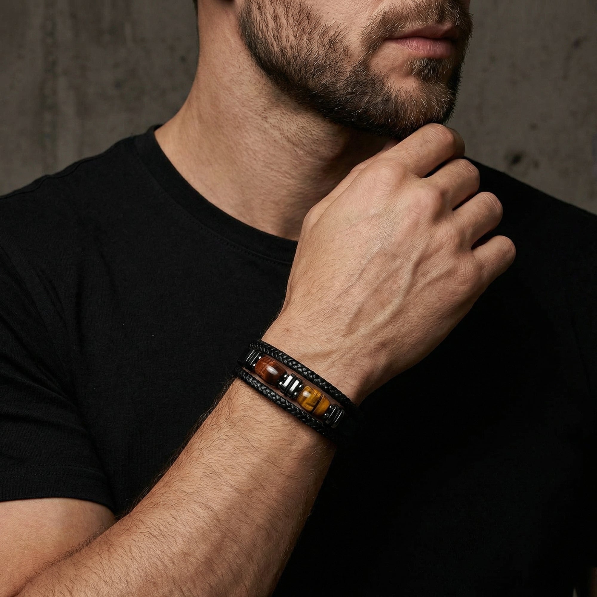 Men's black braided leather and steel bracelet with tiger's eye stones worn on a wrist by a model.