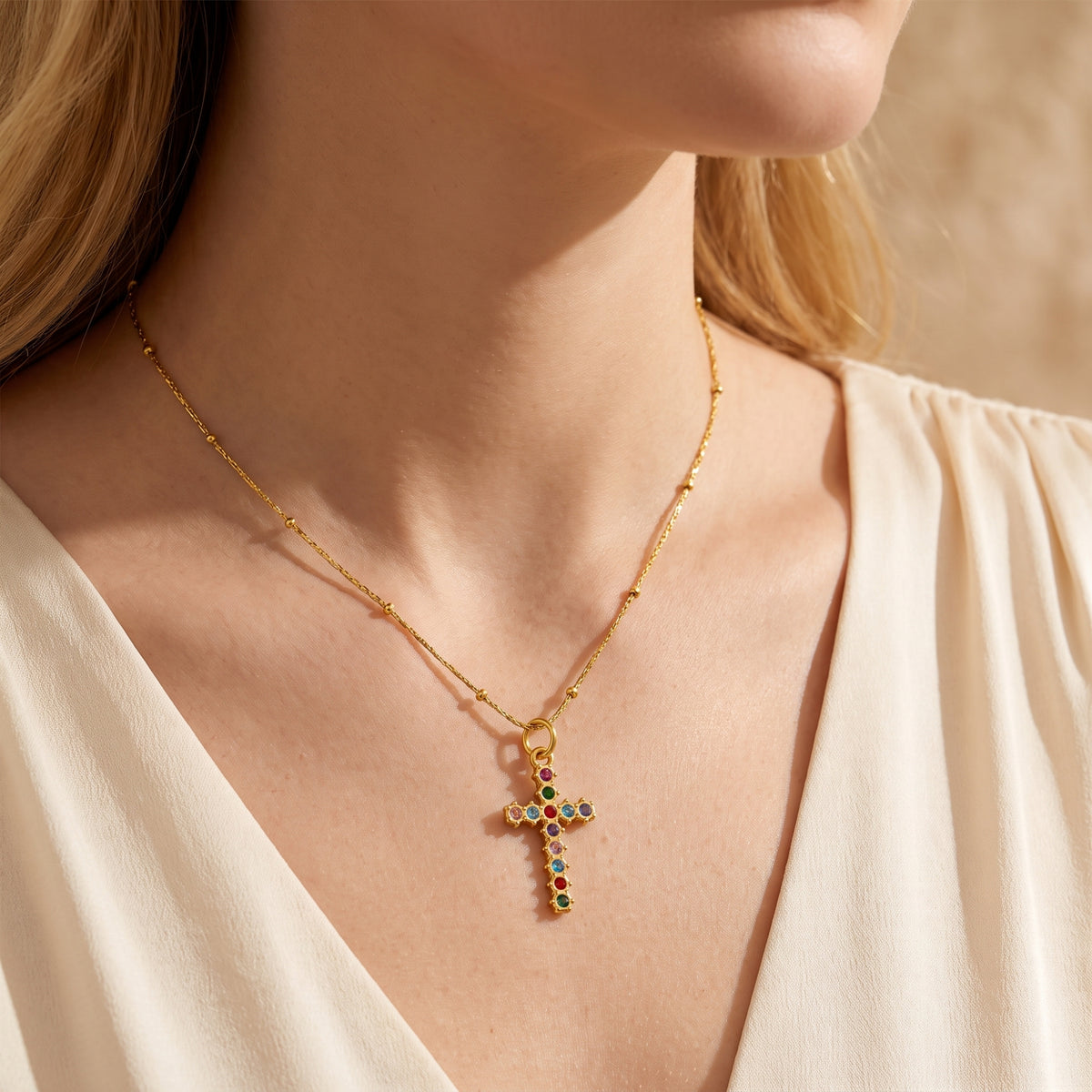 Close-up of a model wearing the gold-tone multicolored cross necklace with a cream V-neck top.