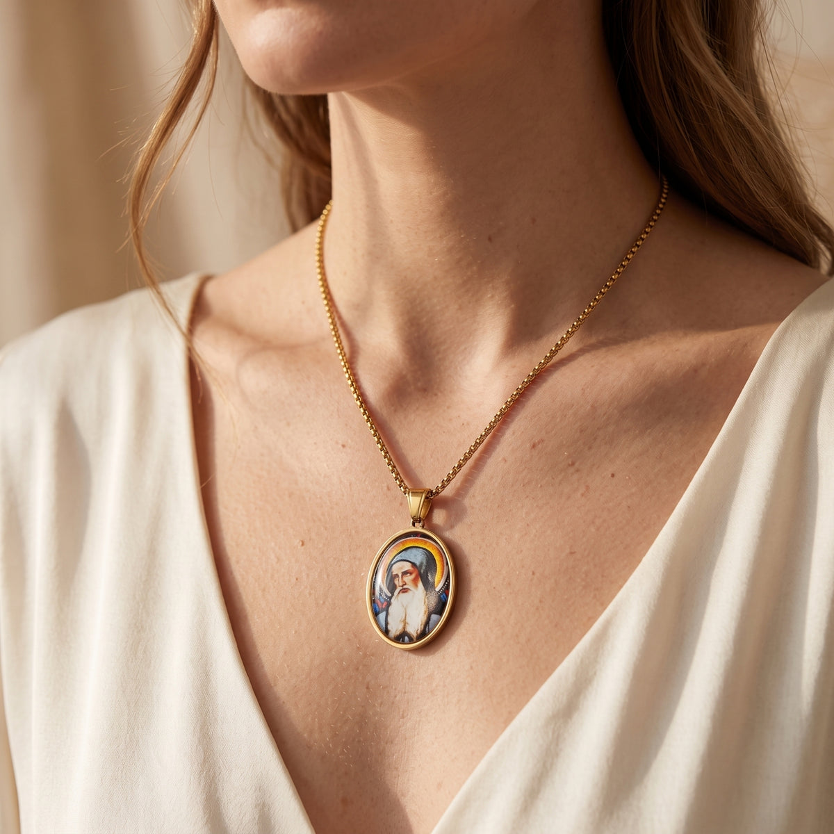 Woman wearing a gold-tone oval saint pendant necklace with a white V-neck top.