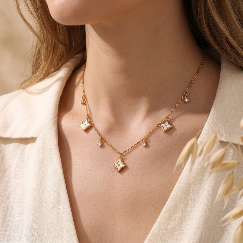 Gold stainless steel necklace featuring white star pendants and crystals worn by a model in a cream shirt.