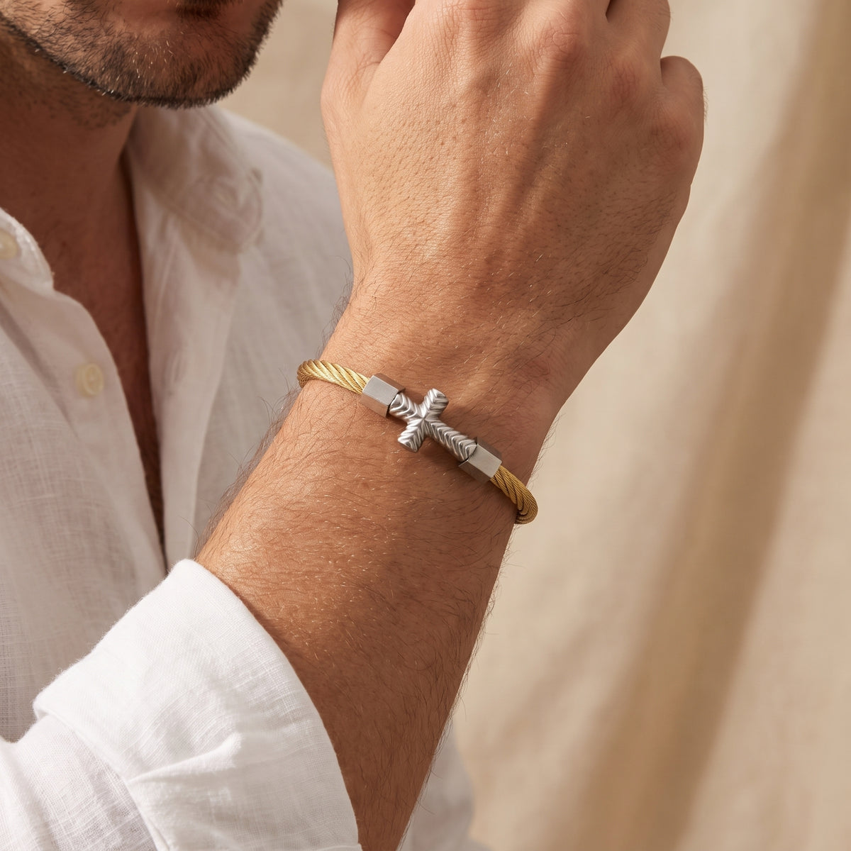 Close-up of a man wearing the gold-tone twisted cable cross cuff bracelet with a white shirt.
