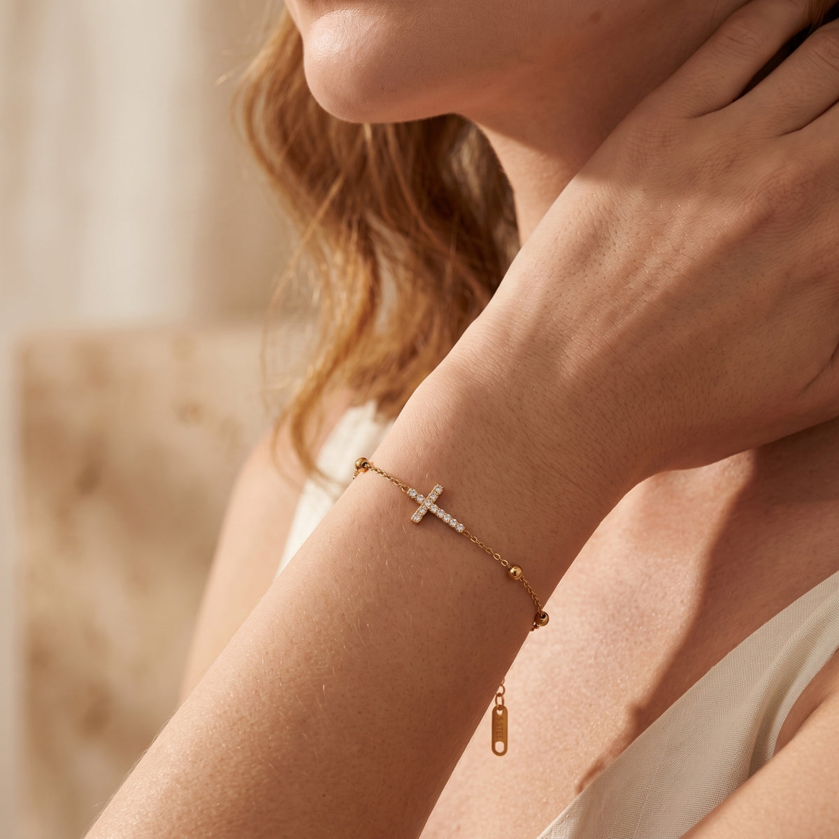 Close-up of a model wearing the gold-tone pave cross bracelet on her wrist with her hand near her neck.