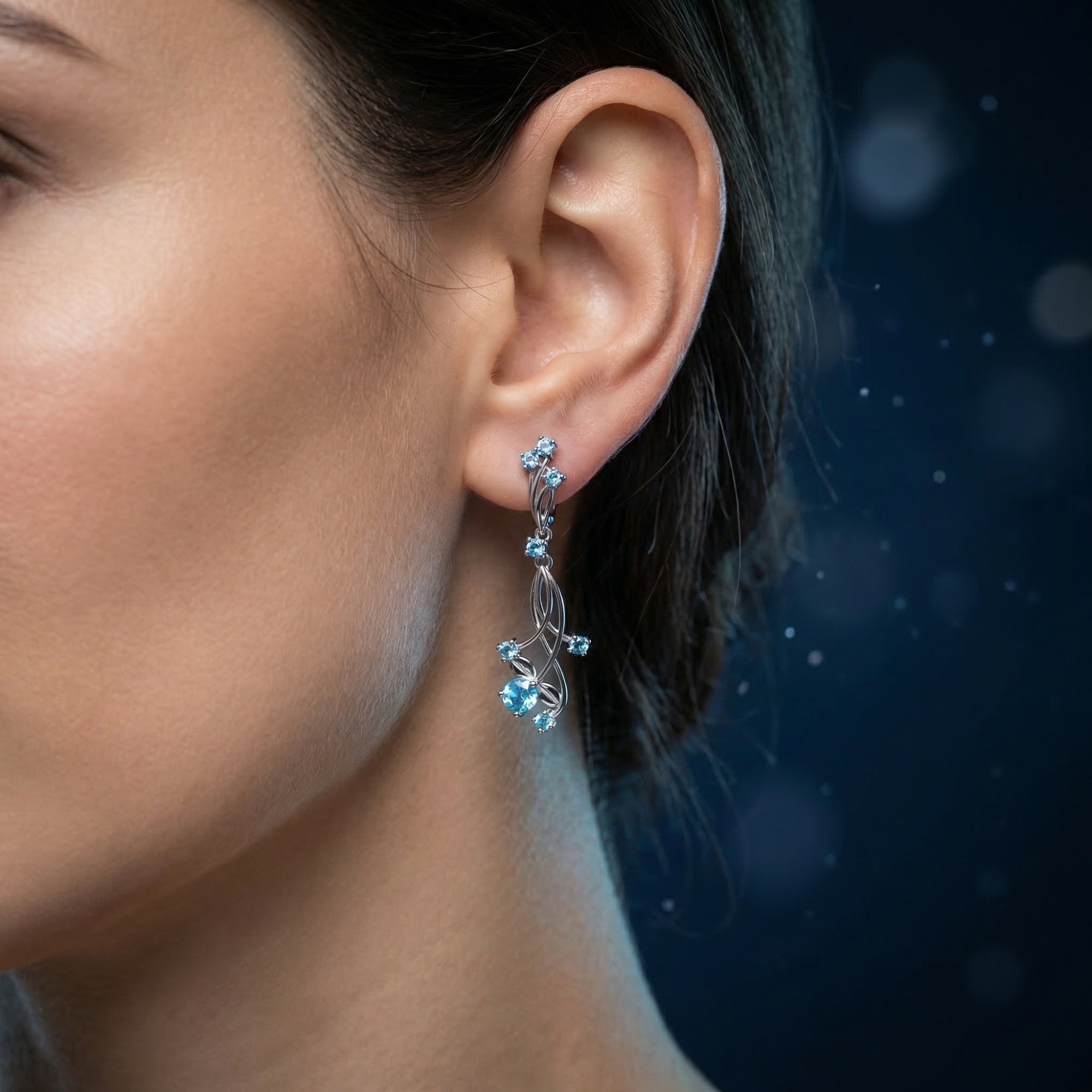 Side view of a model wearing an Oceanis Cascade silver blue topaz drop earring with a cascading vine design.