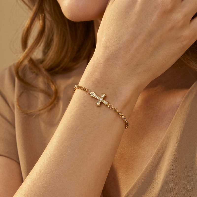 Close-up of a wrist wearing a gold-tone cross bracelet with sparkling stones.