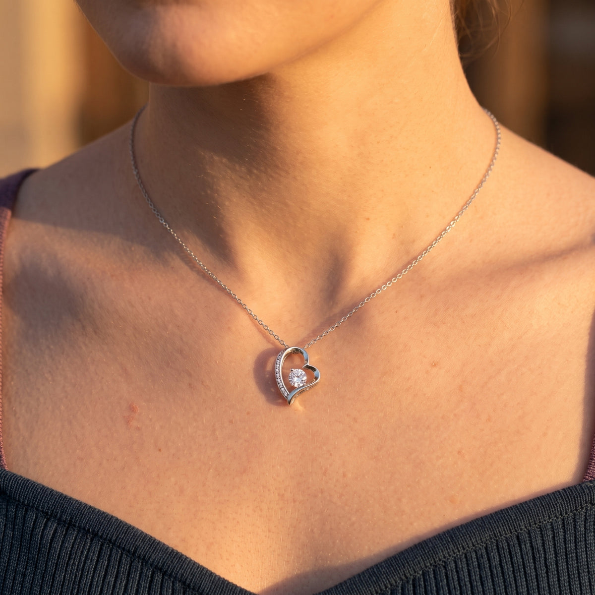 Silver-finish heart necklace worn at the neckline.