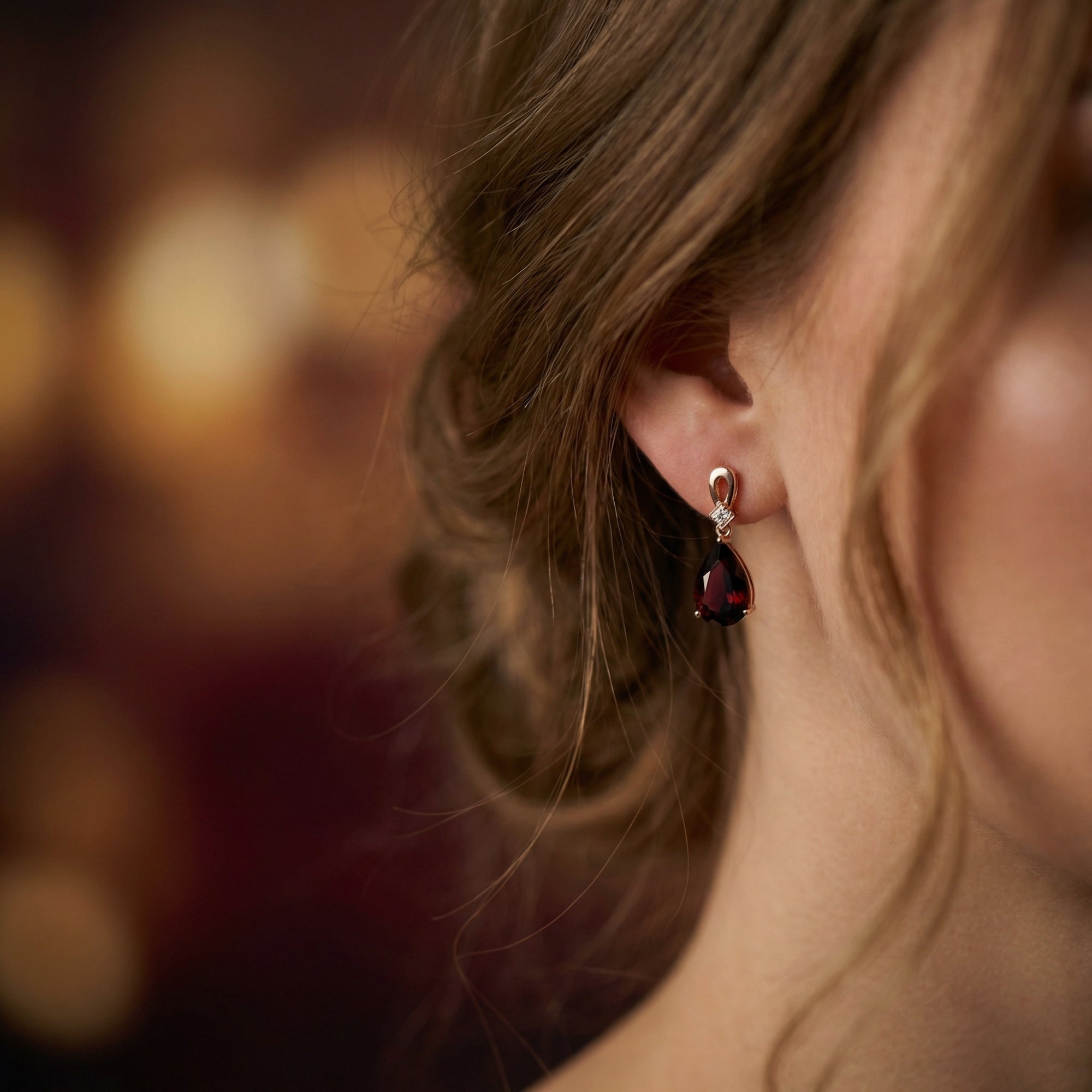 Model wearing an 18K rose gold drop earring featuring a large pear-cut garnet against a soft-focus background.