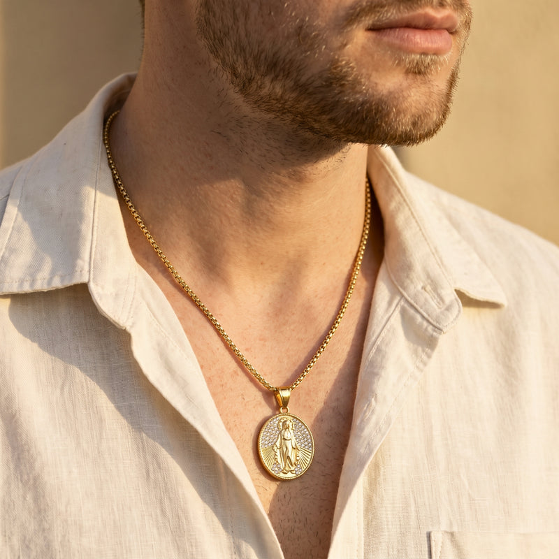 Man wearing a gold-tone oval Miraculous Medal necklace centered over an open white shirt.