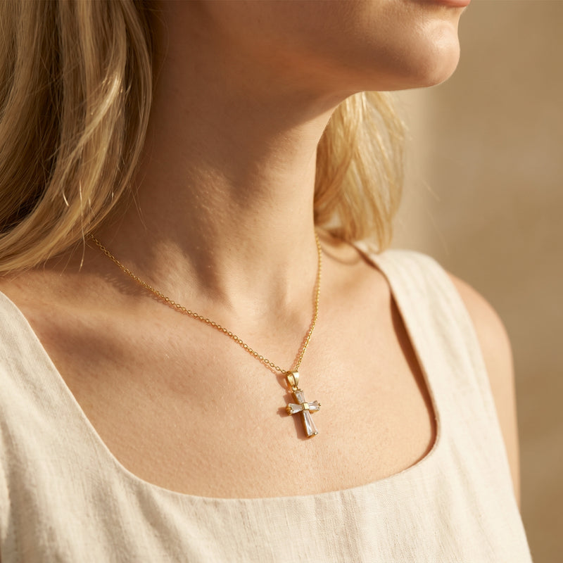 Close-up of a model wearing the gold baguette cross necklace over a cream sleeveless top.