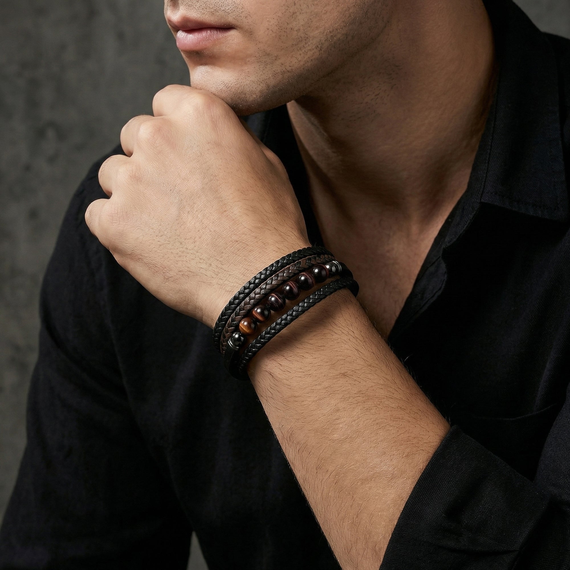The Maverick leather bracelet with red tiger's eye beads worn on a man's wrist with a black button-down shirt.