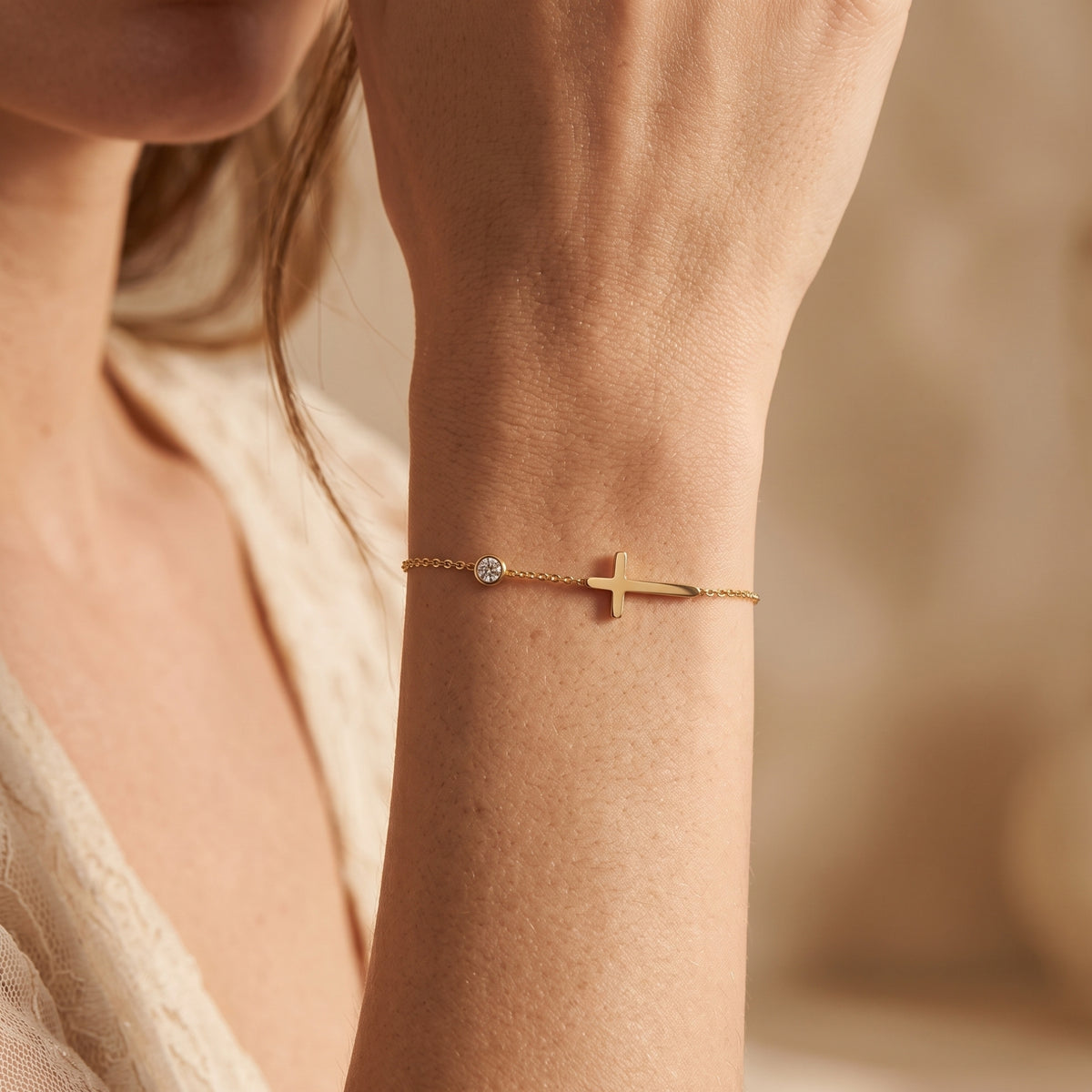 Close-up of the gold-tone sideways cross bracelet with a round clear stone worn on a woman's wrist.