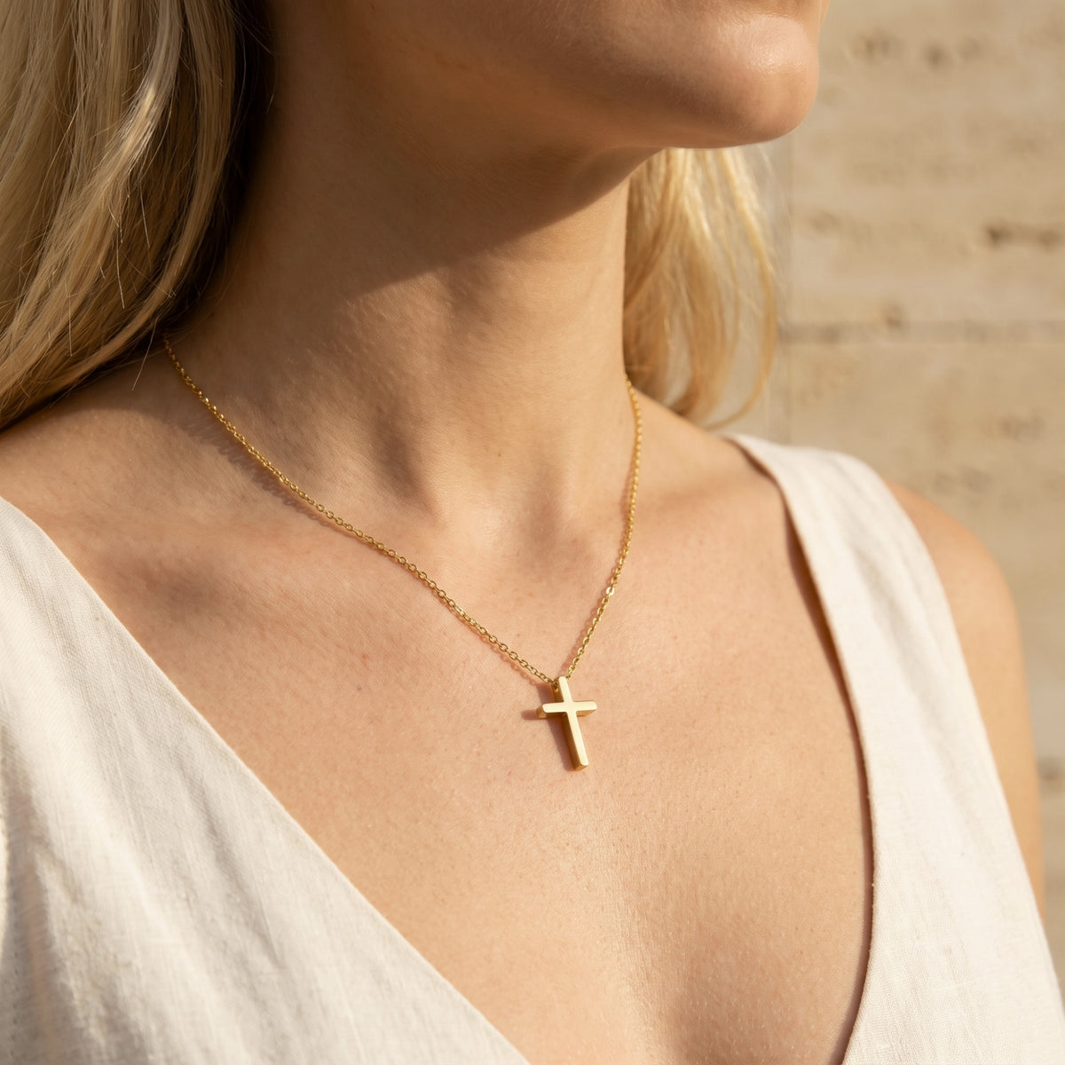 Close-up of a woman wearing a gold-tone cross necklace with a thin chain over a white sleeveless top.