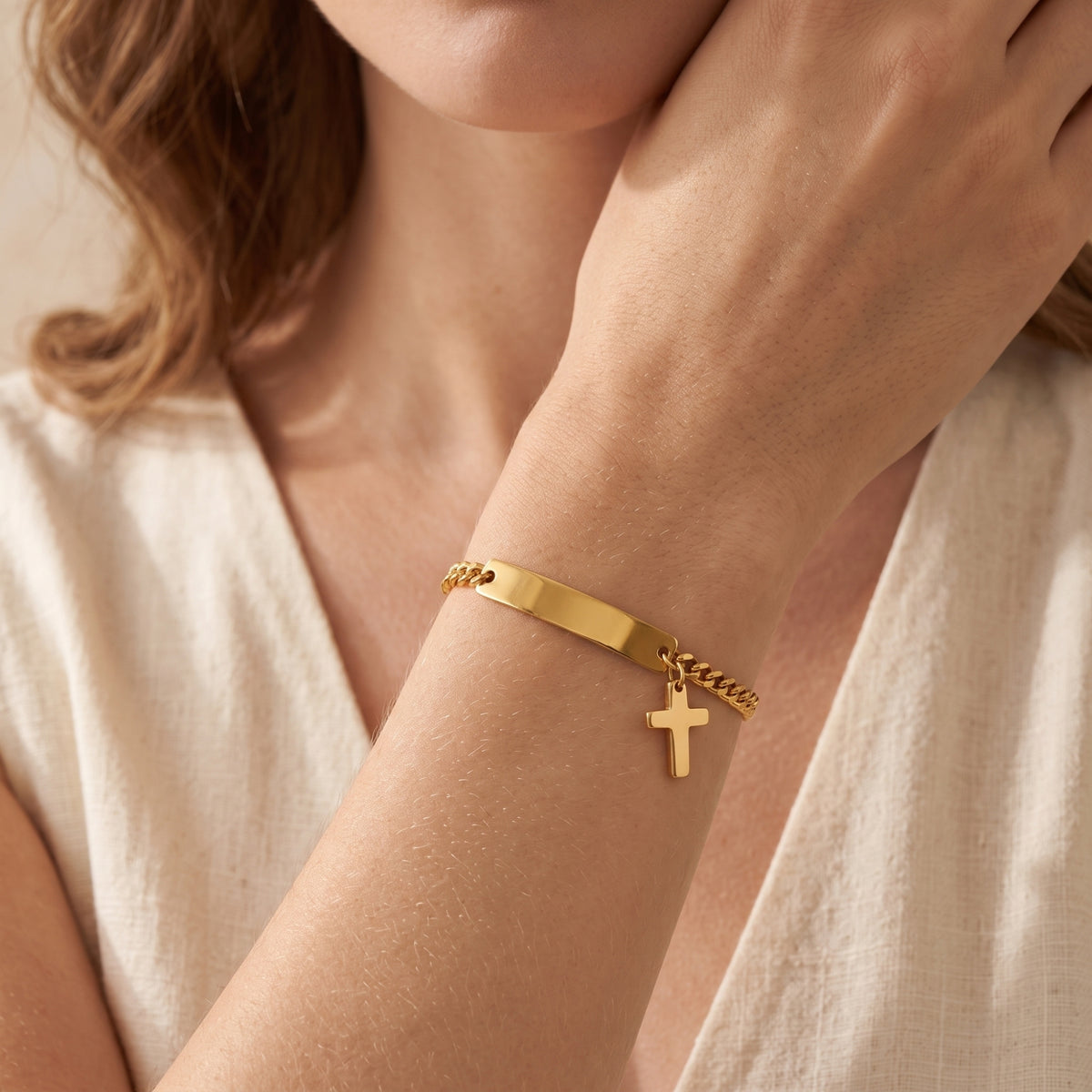 Woman wearing the gold-tone cross ID Figaro bracelet on her wrist with a cream outfit.