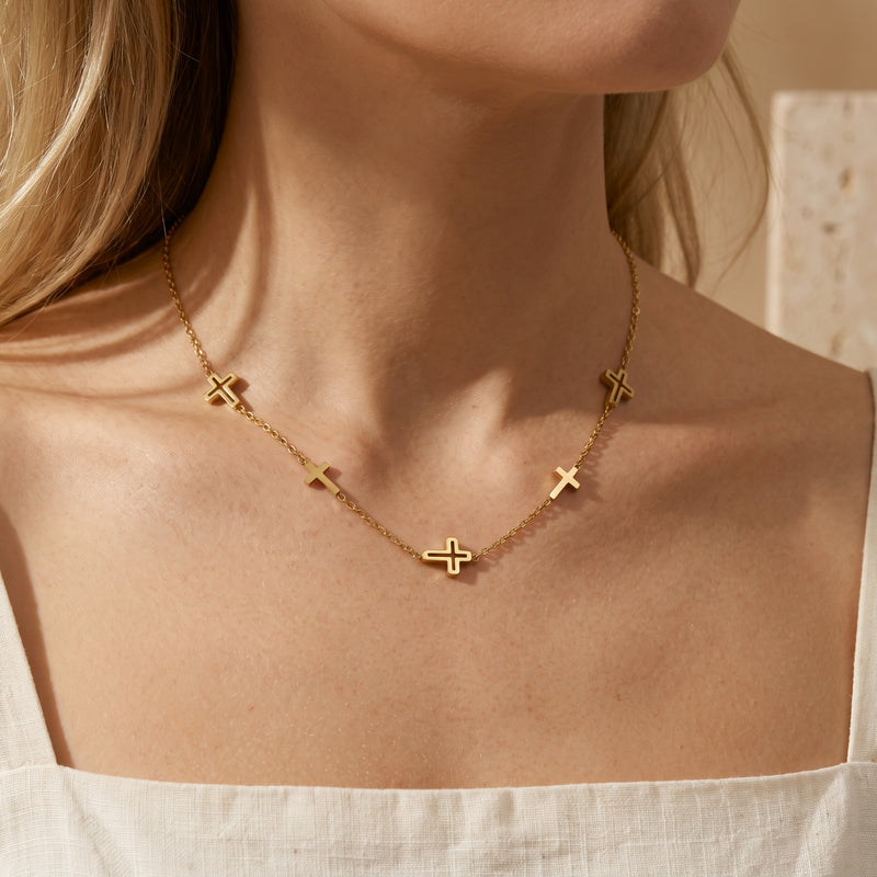 Model wearing a gold-tone multi-cross station necklace with a white square-neck top.