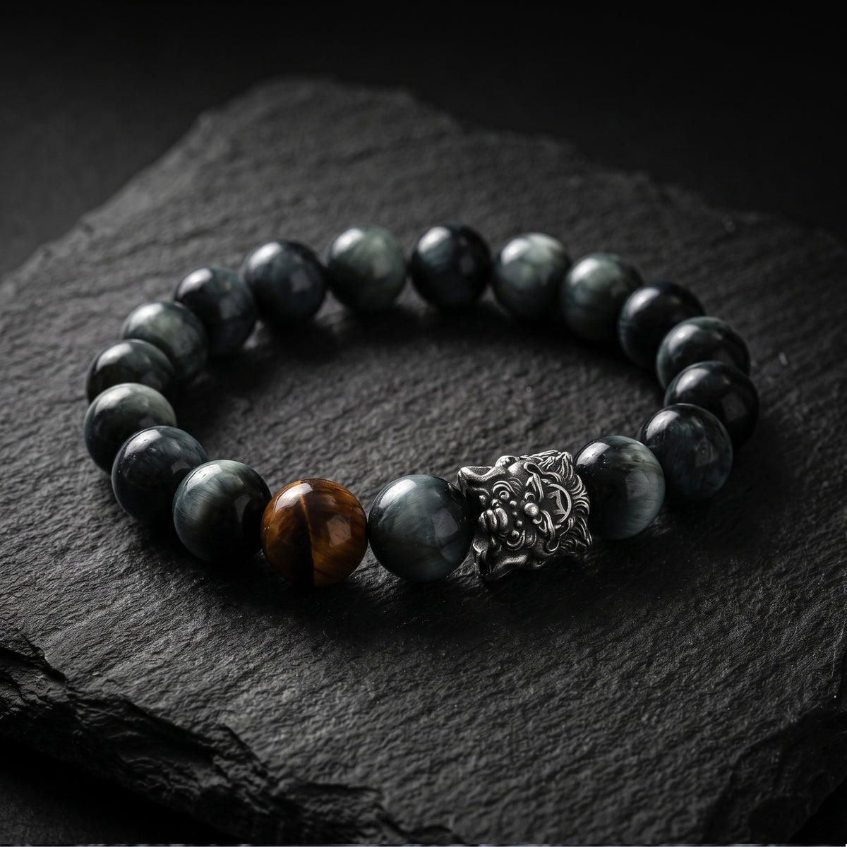 Angled close view of a silver lion charm and chatoyant dark beads on black slate.