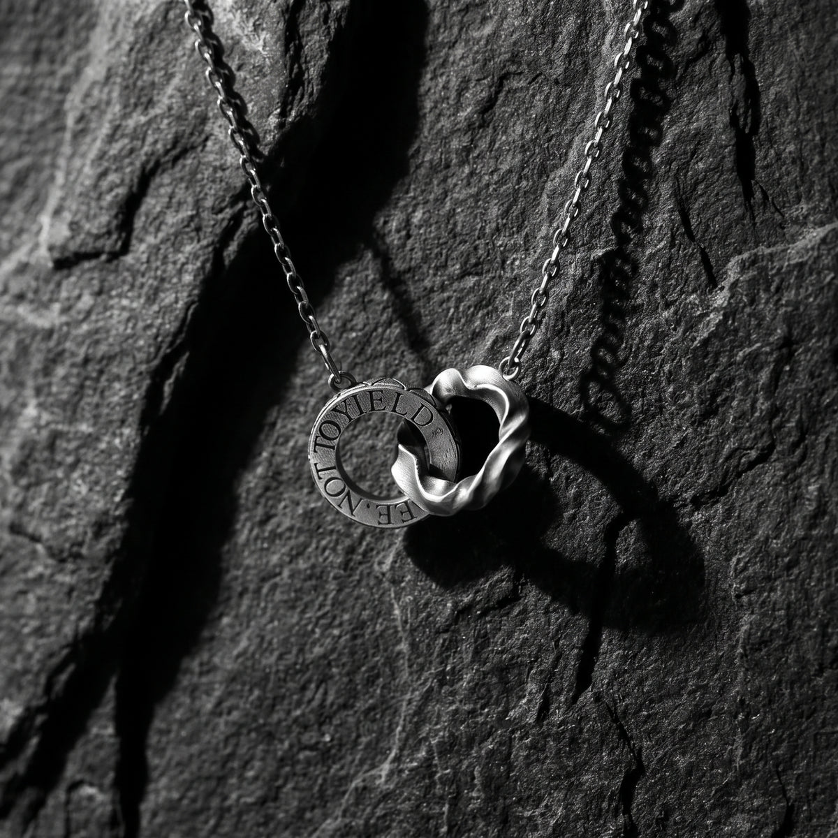 Front-facing view of the silver dual-ring pendant and chain resting on a dark slate surface.
