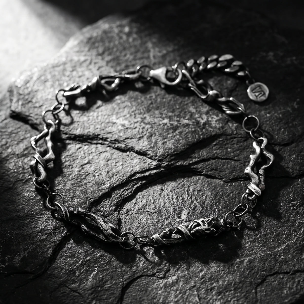 Full view of the oxidized silver bracelet arranged in an open loop on dark slate, showing textured sculpted links.
