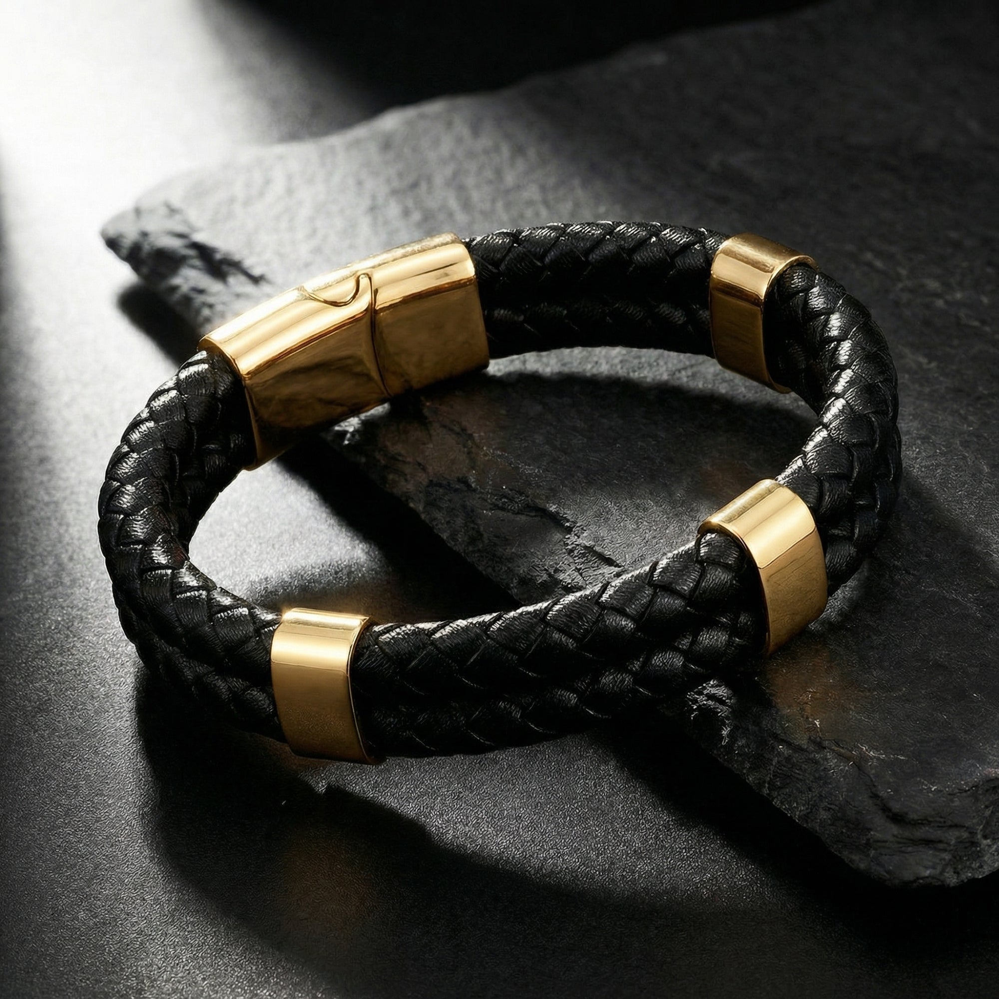 Close-up of a braided black leather bracelet with a gold magnetic clasp on a dark slate background.