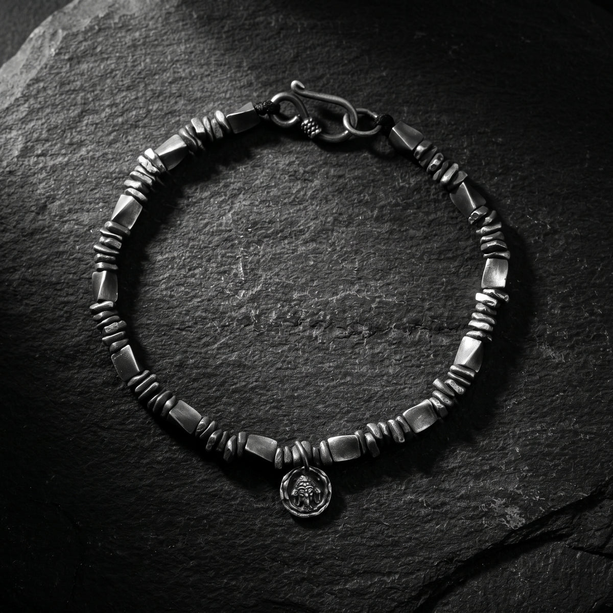 Top-down view of the circular silver textured link bracelet with S-hook clasp on dark stone.
