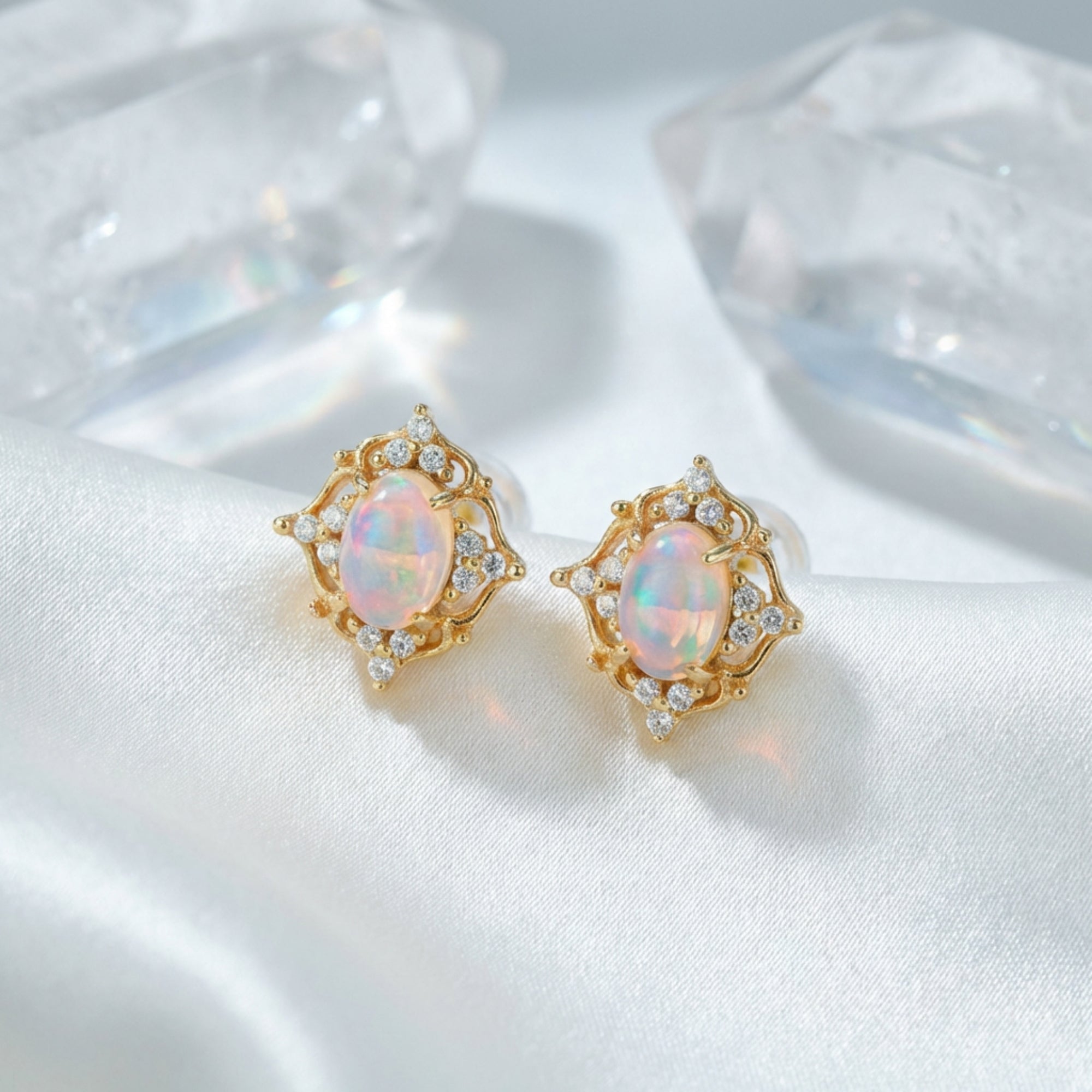 Pair of gold-tone white opal earrings with clear stone accents displayed on white silk with crystal props.