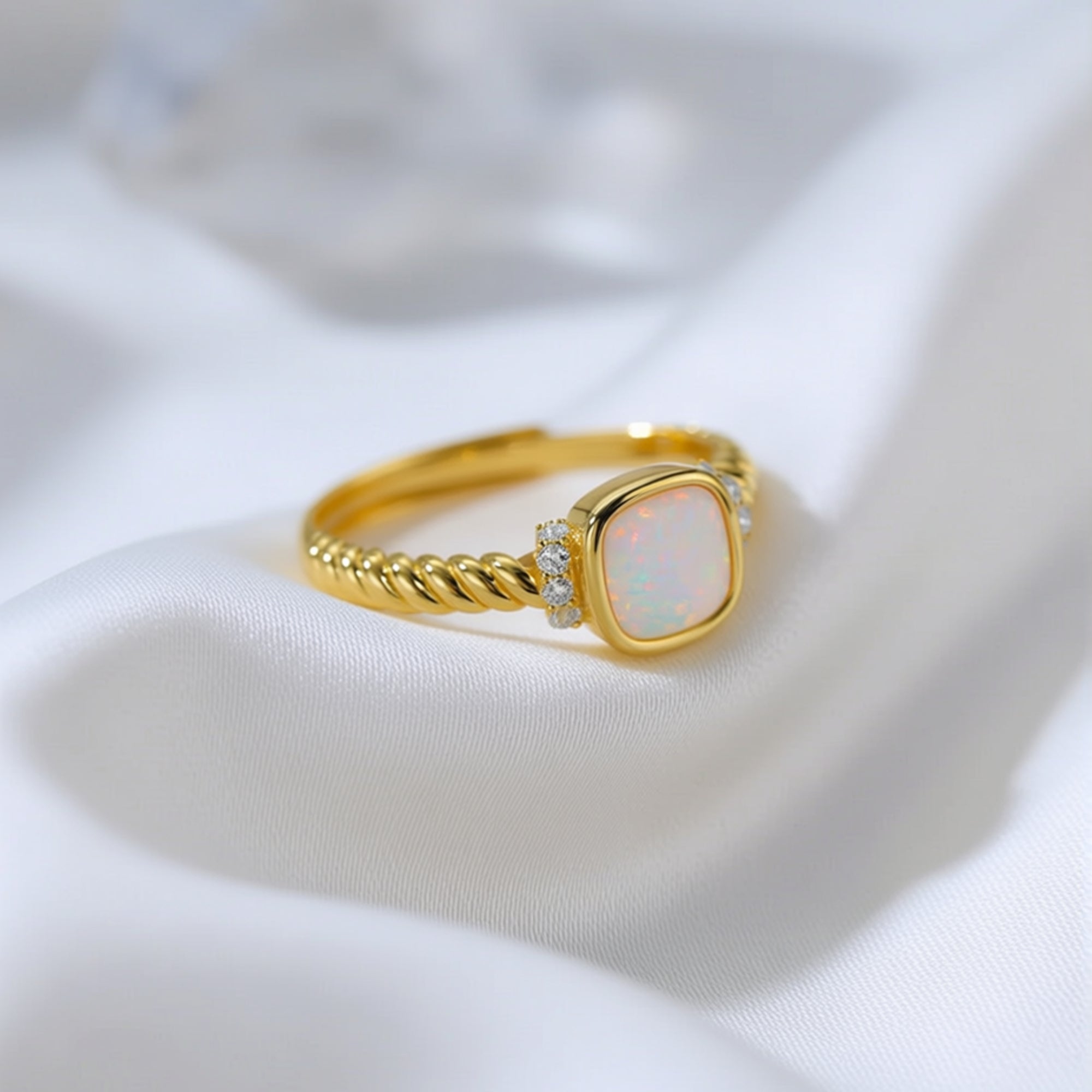 Macro view of the gold-tone twisted band and cushion-cut white opal with sparkling side stone accents.