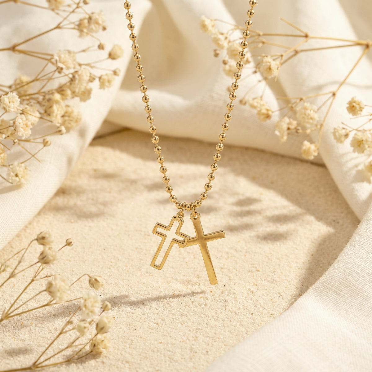 Gold-tone double cross necklace hanging above sand, with solid and open outline cross pendants.