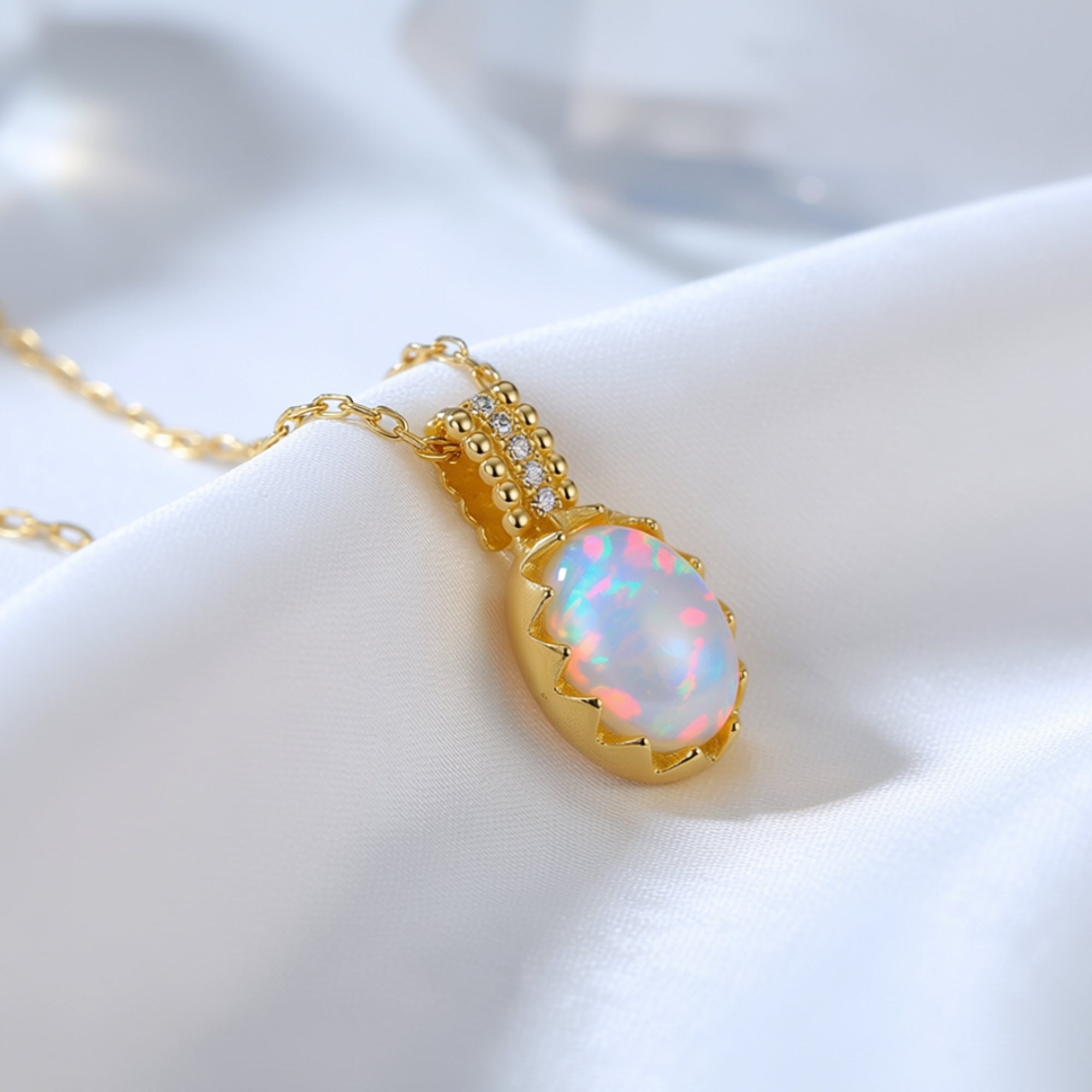 Close-up of the gold-tone Orianthi pendant showing the iridescent play-of-color in the oval white opal stone.