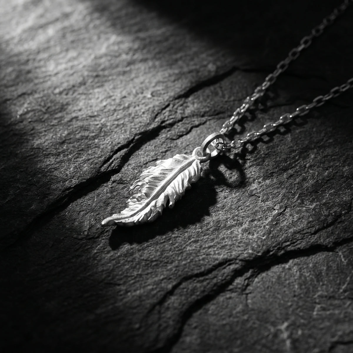 Close-up view of the detailed silver feather pendant resting on a dark slate surface.
