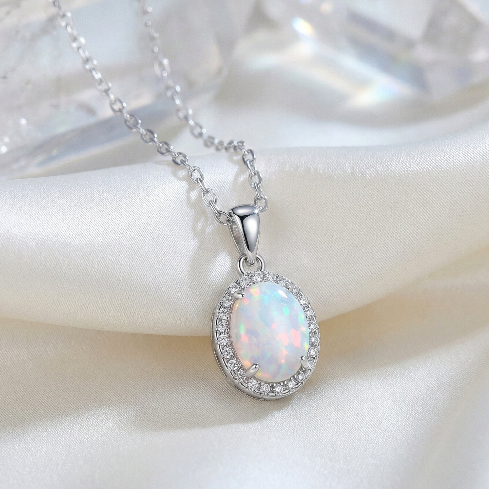 S925 sterling silver necklace with a dainty oval cut white opal pendant, displayed on white silk fabric.