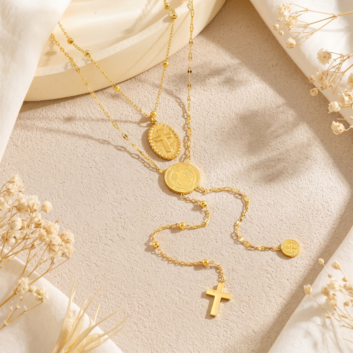 Top-down view of the gold-tone layered necklace with cross medallion, round medal, and dangling cross on beige fabric