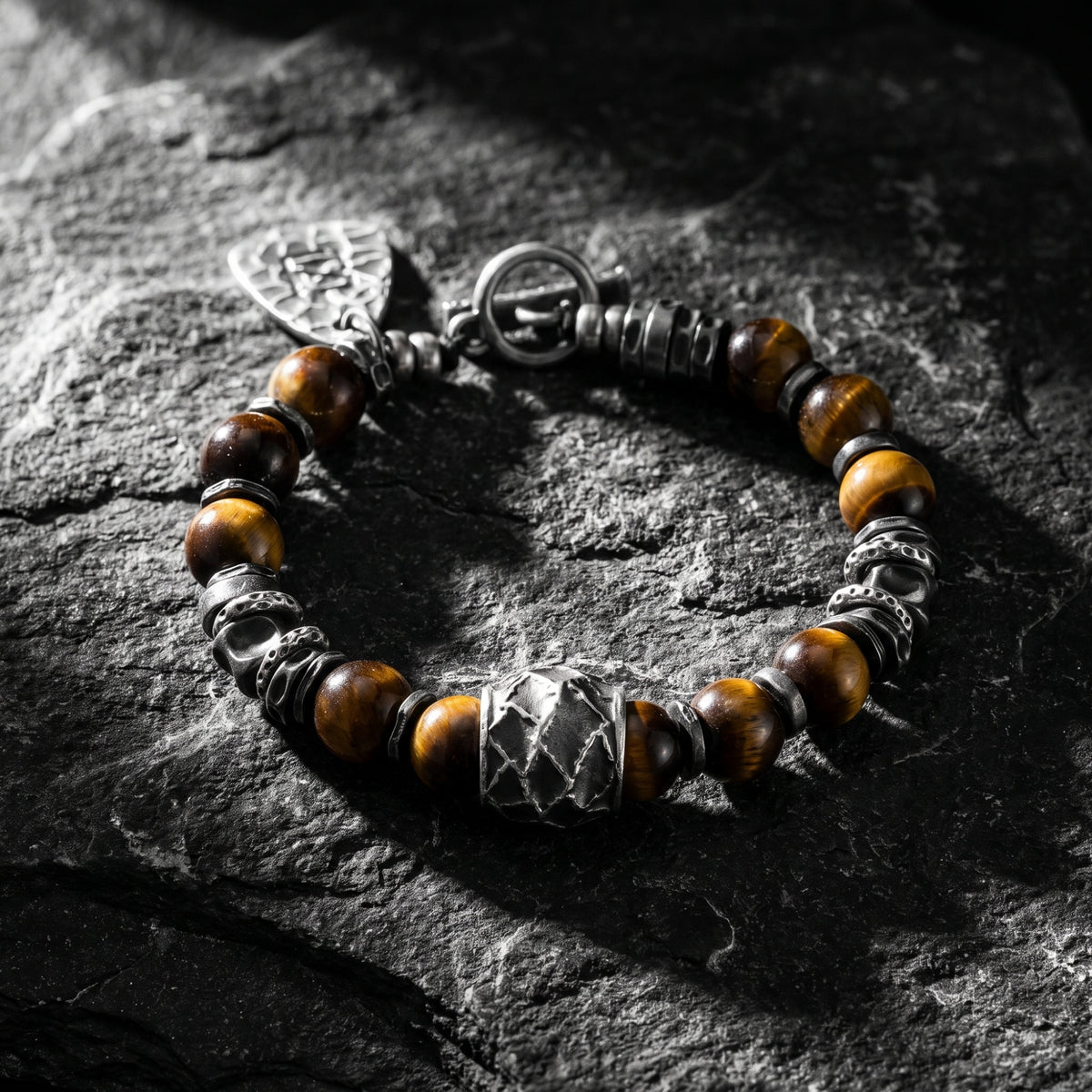 Beaded bracelet on rough dark stone, showing a large carved silver focal bead and brown tiger's eye beads.