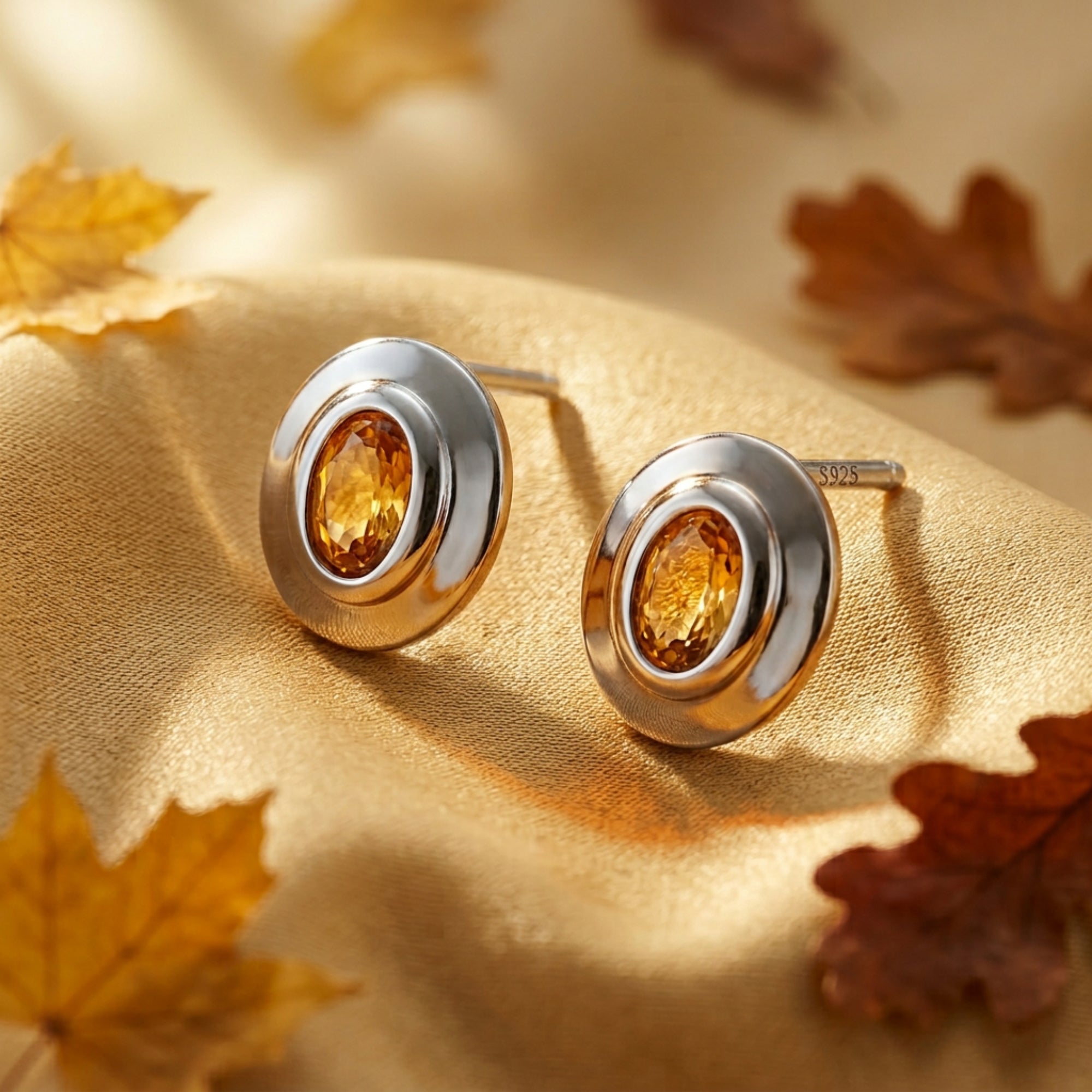 Detail shot of silver oval cut citrine earrings with S925 engraving on gold fabric.