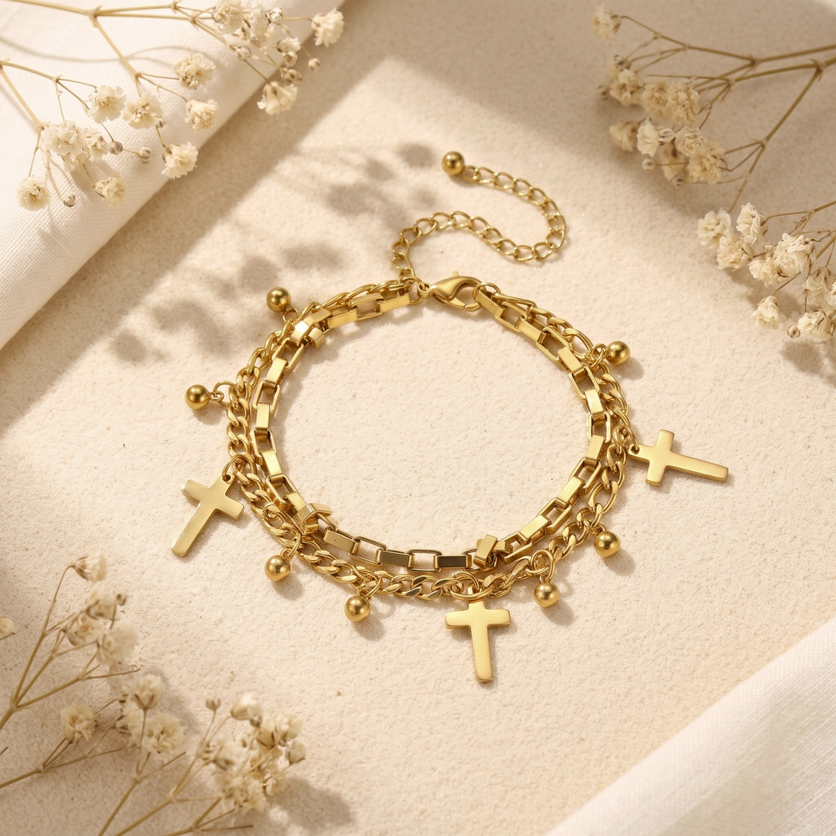 Top-down view of the gold-tone double-layer bracelet with cross and bead charms, clasp, and extender chain visible.
