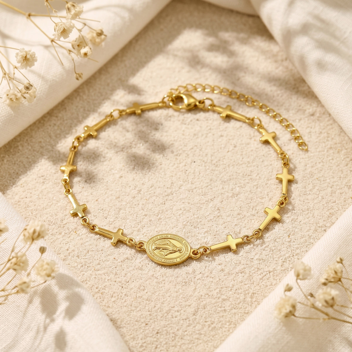 Overhead view of the gold-tone cross station bracelet with central oval medal framed by white fabric.