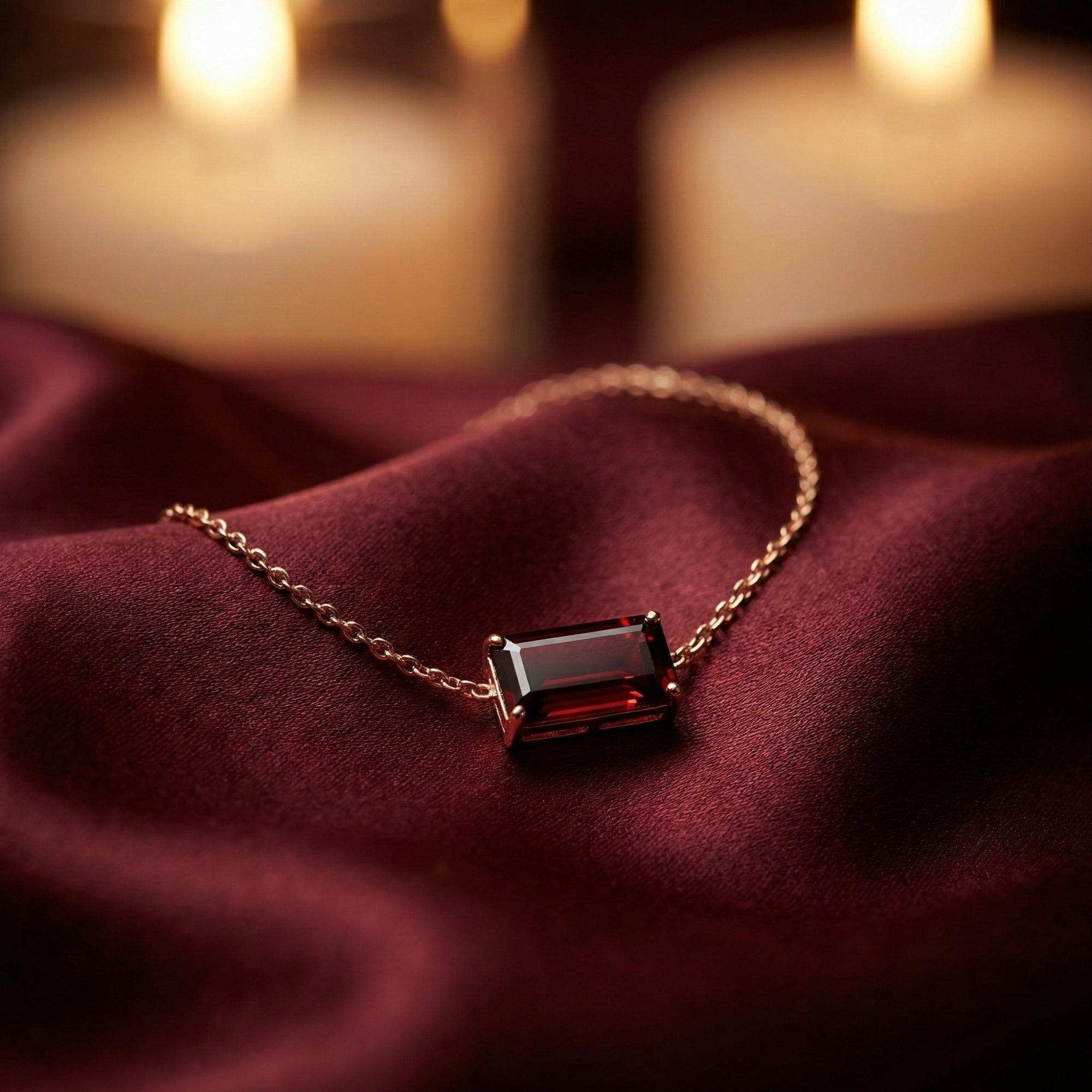 Detail shot of a 1.6-carat emerald-cut natural garnet in an 18K rose gold setting on dark burgundy fabric.