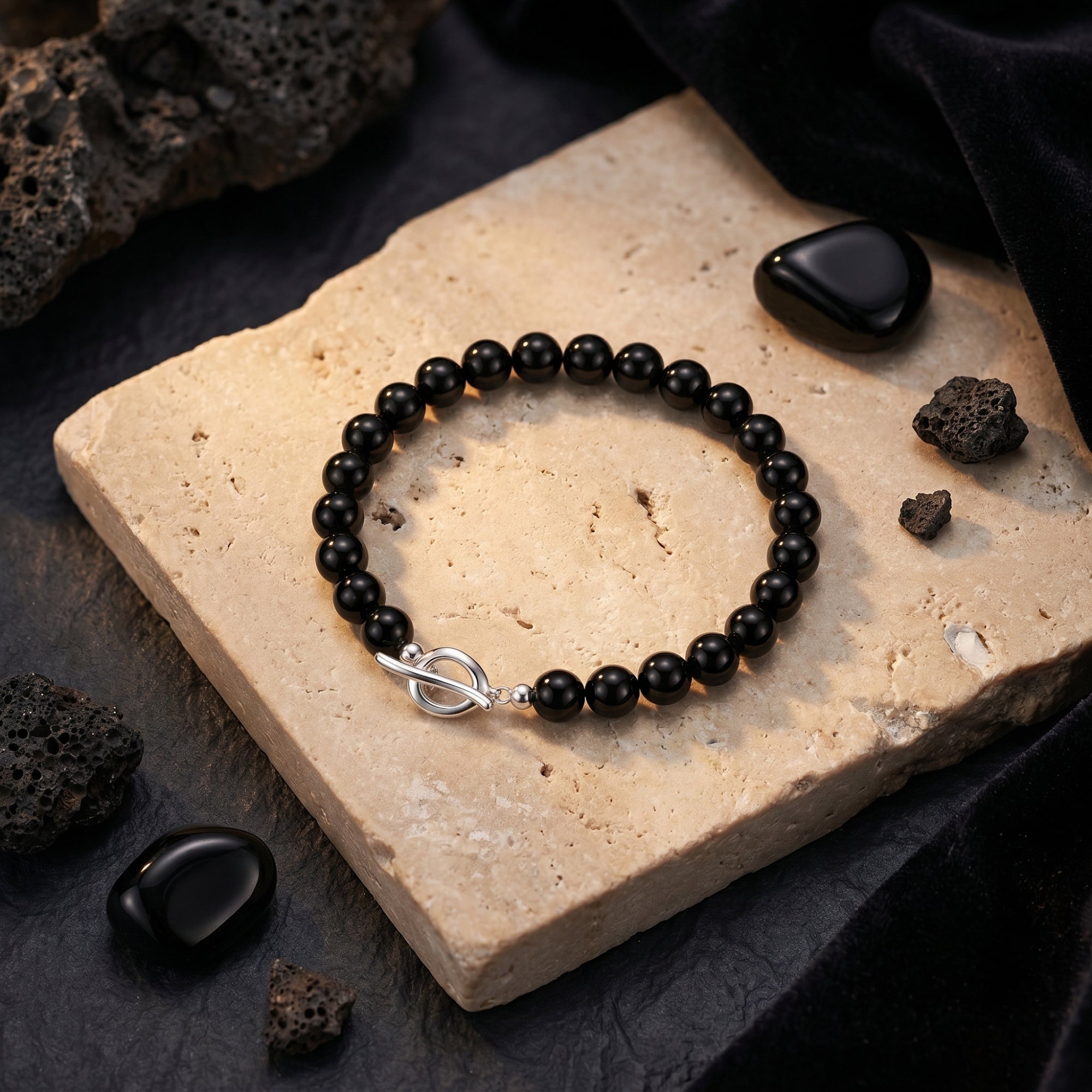 Solumbra onyx bead bracelet with a silver toggle clasp displayed on a textured stone surface with black rocks.
