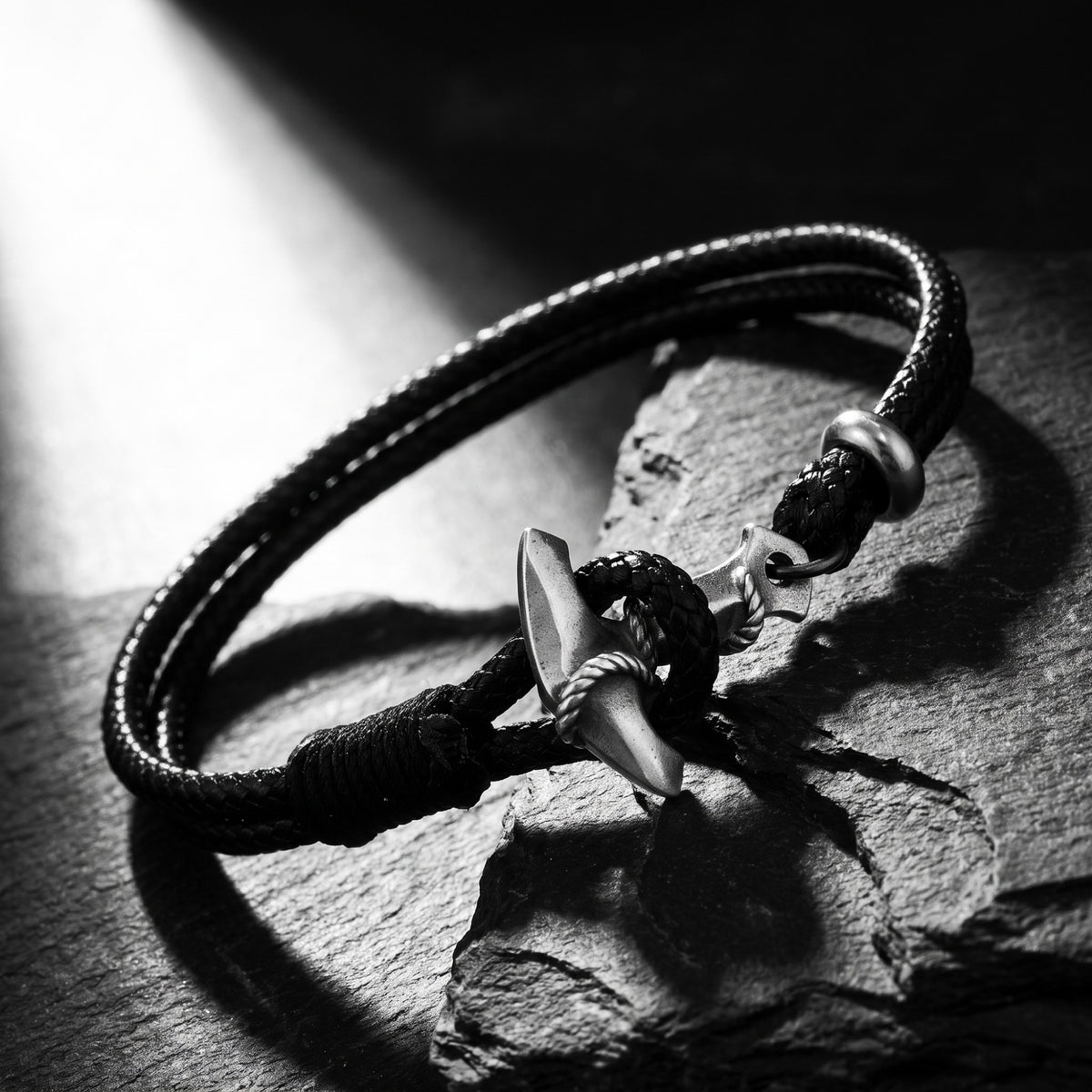 Angled view of a black cord anchor bracelet resting on a textured slate rock.