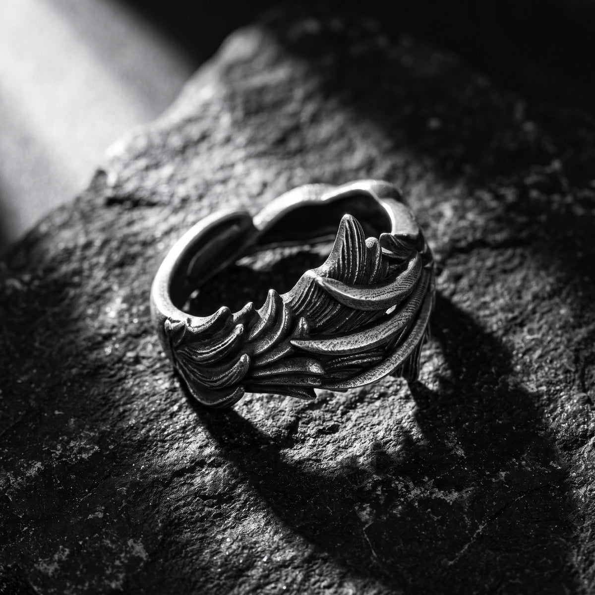 Angled silver feather open band ring resting on textured rock, with its inner band visible.