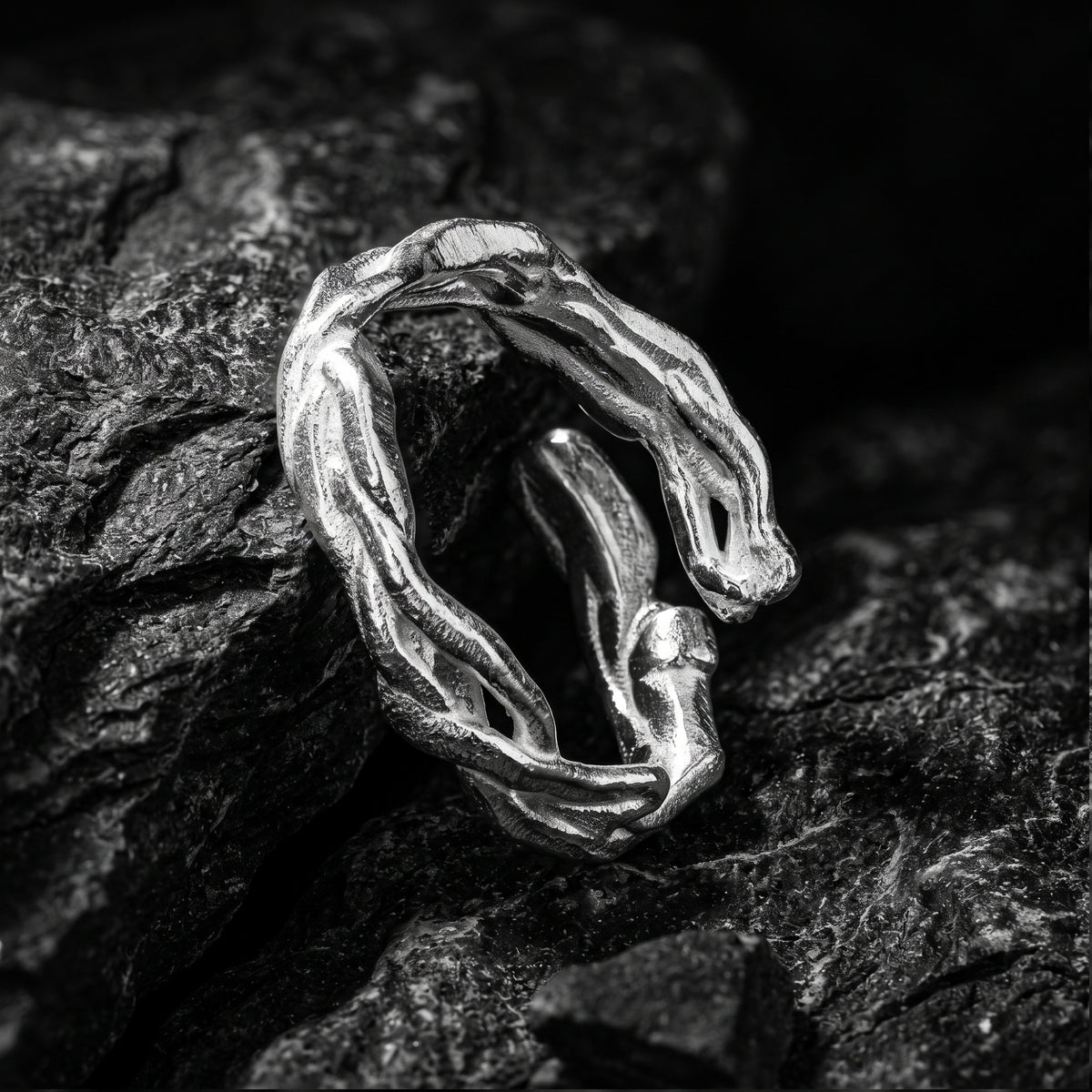 Upright close-up of the silver open ring with sculpted strands leaning among dark textured rocks.