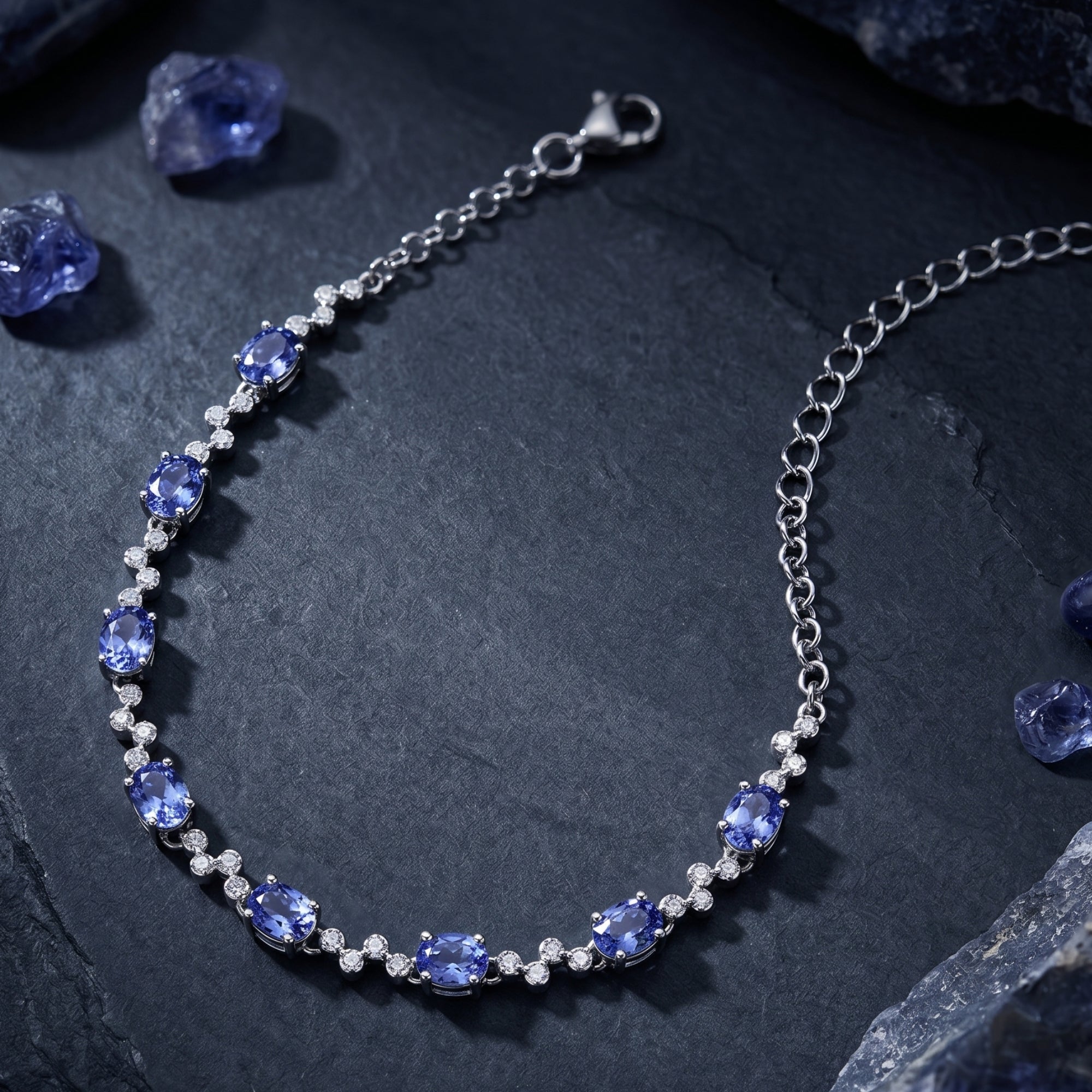 Sterling silver station bracelet featuring oval natural tanzanite stones laid flat on a textured dark surface.