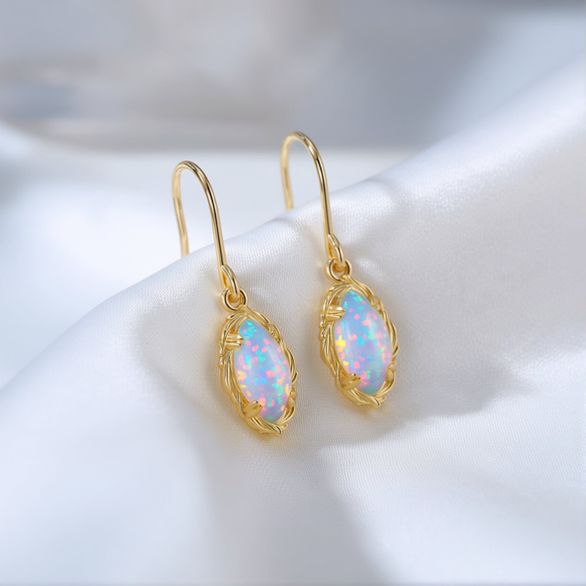 Detailed view of yellow gold drop earrings with marquise-cut white opals showing vibrant color play on white silk.