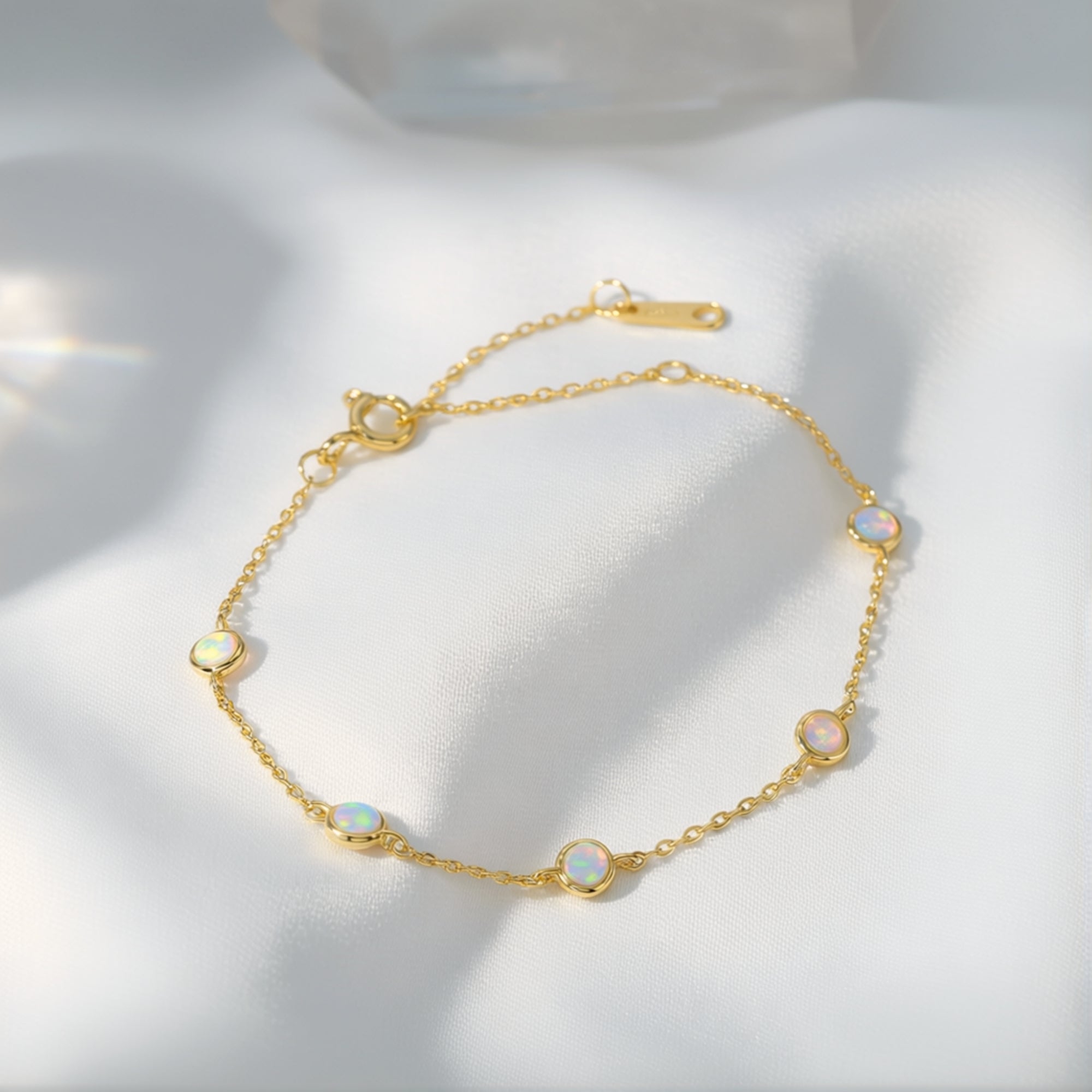 Kyriella gold-tone station bracelet featuring five round cut opals on a draped white fabric background.