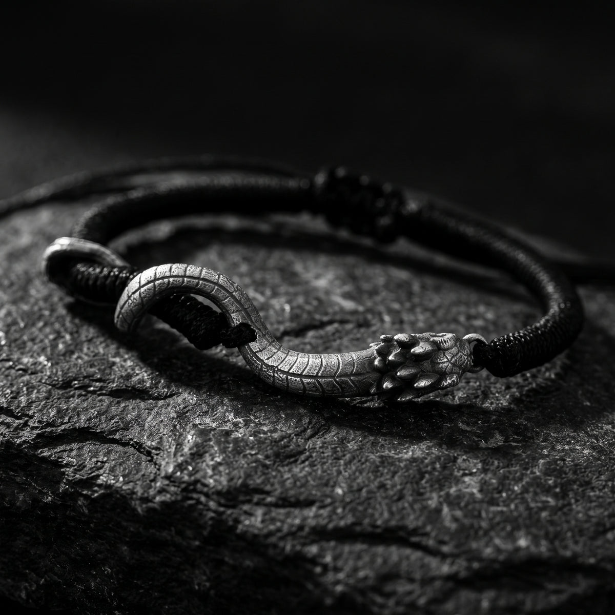 Close-up of the textured silver serpent head and curved body on a black cord bracelet.