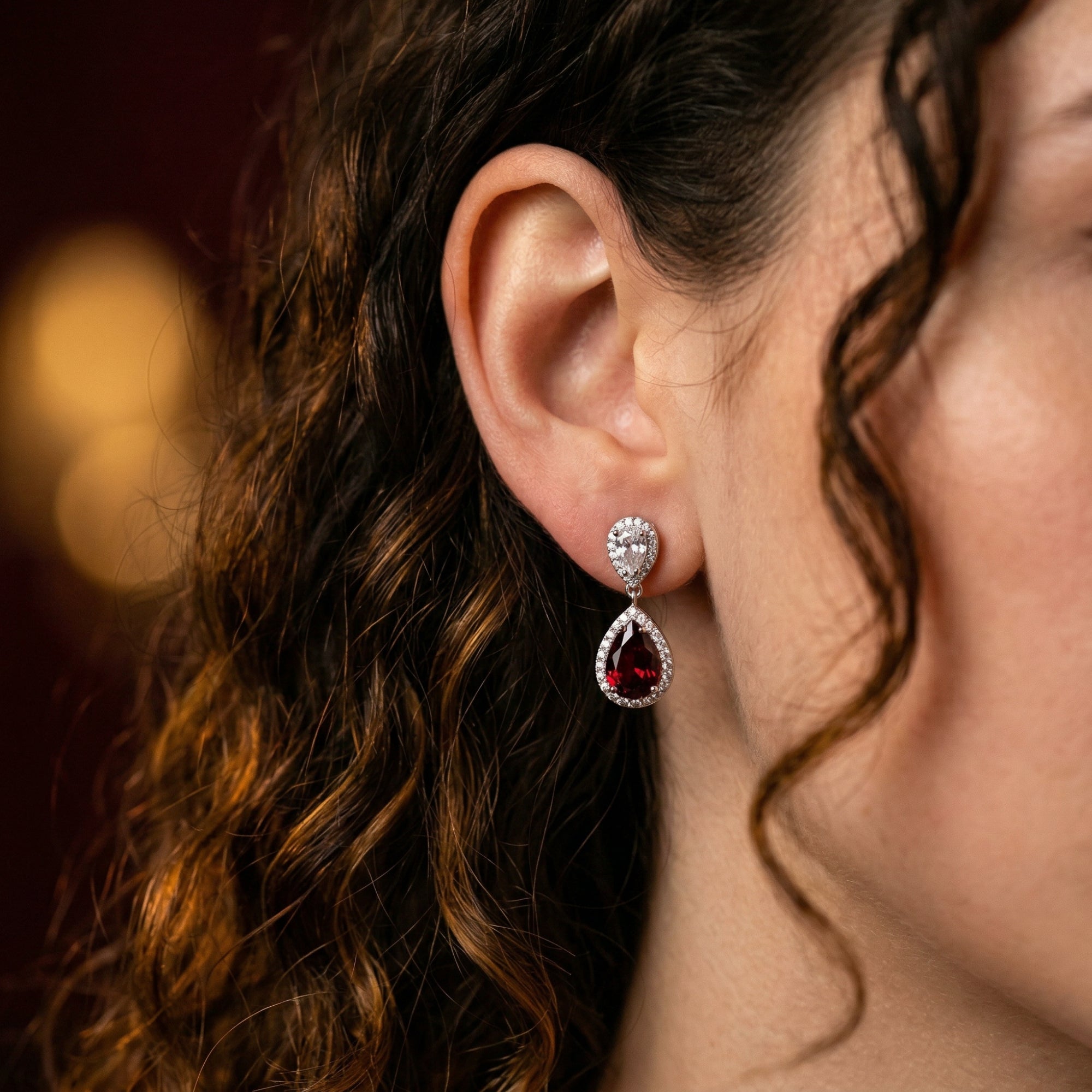 Rosaria drop earring with a pear-cut red garnet and silver halo setting worn on a model's ear.