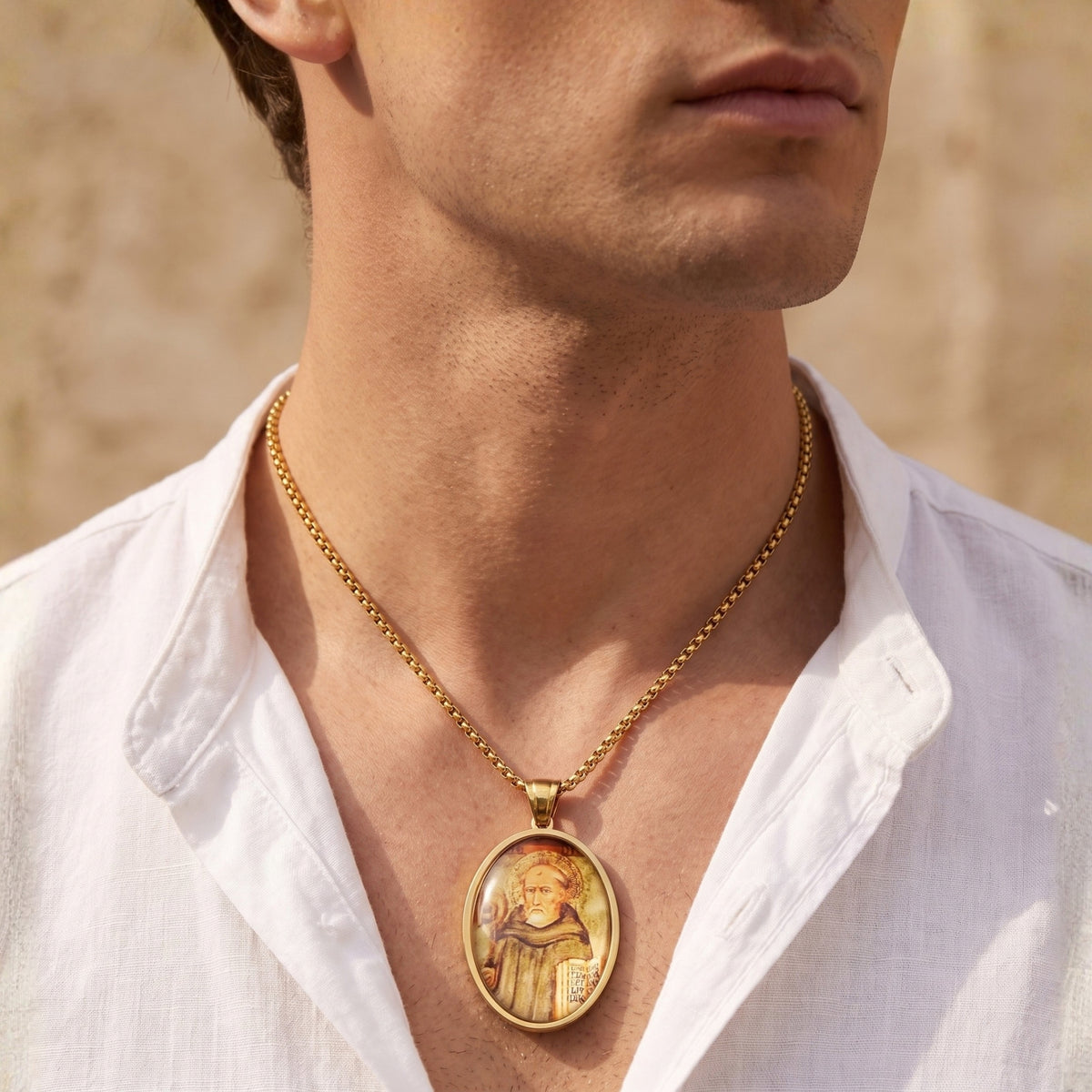 Close-up of a man wearing the gold-tone oval saint icon pendant necklace over an open white shirt.