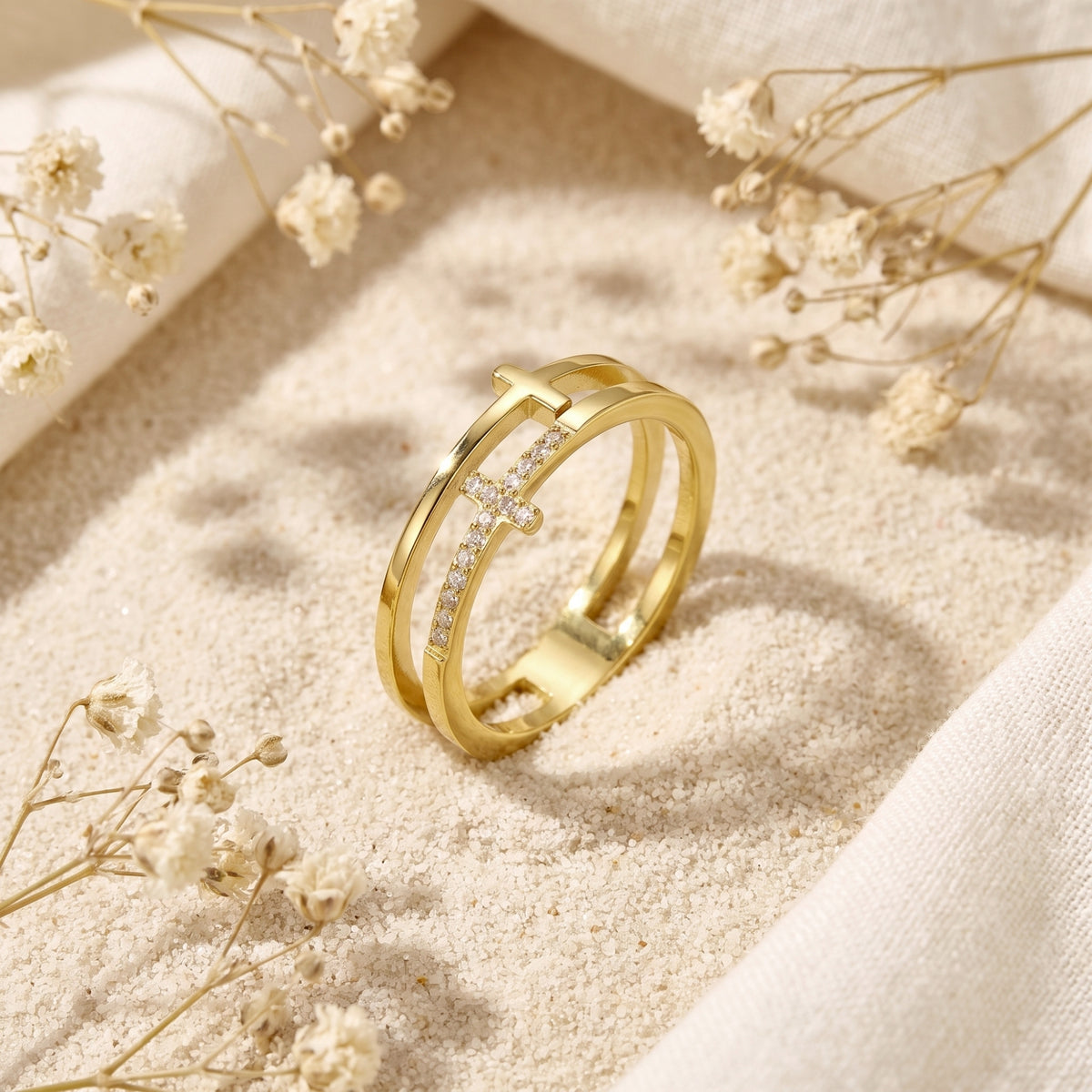Angled gold dual-band cross ring standing on sand, showing its open space and crystal-set cross.
